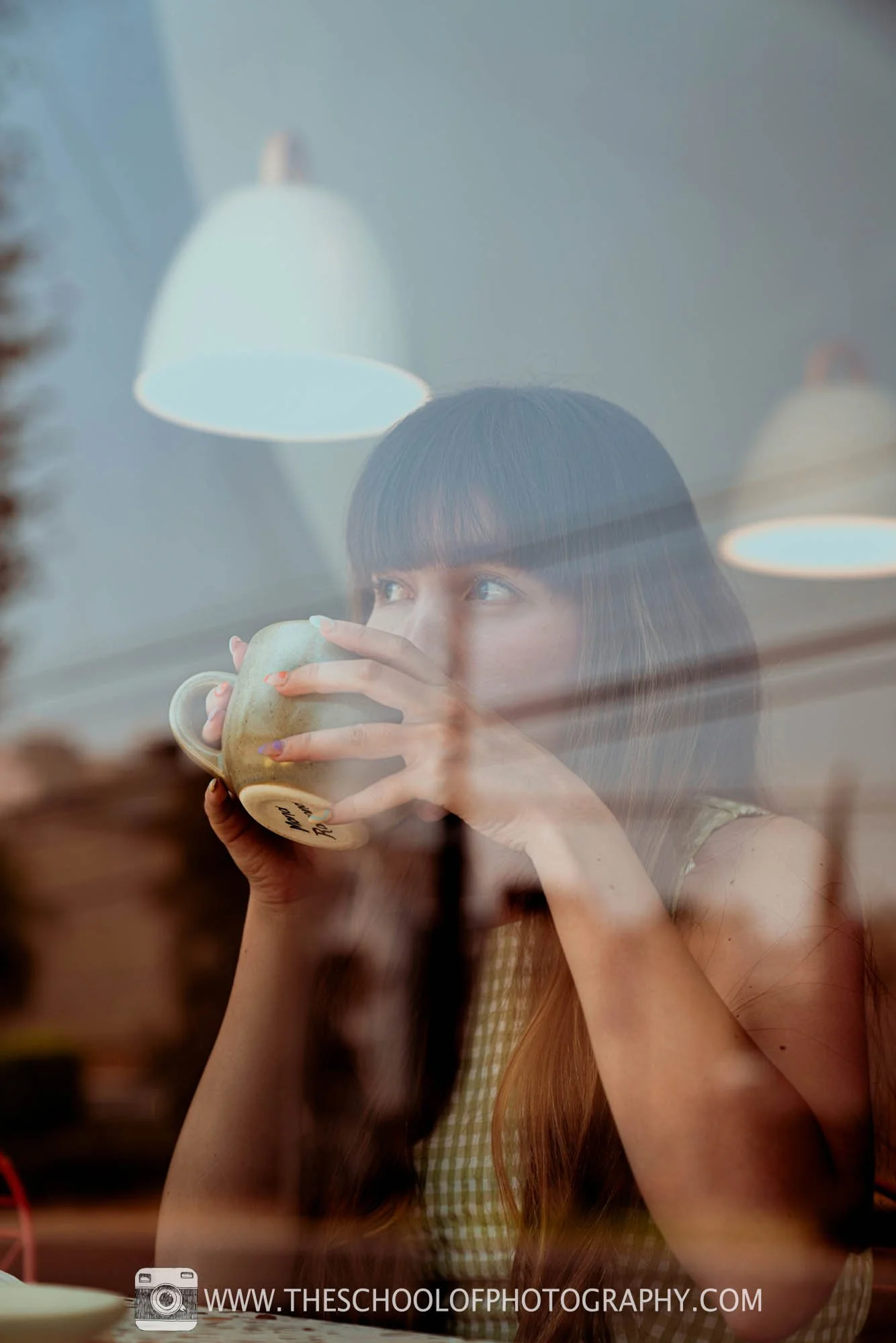 image of a woman drinking coffee in a cafe, viewed through a window with reflection