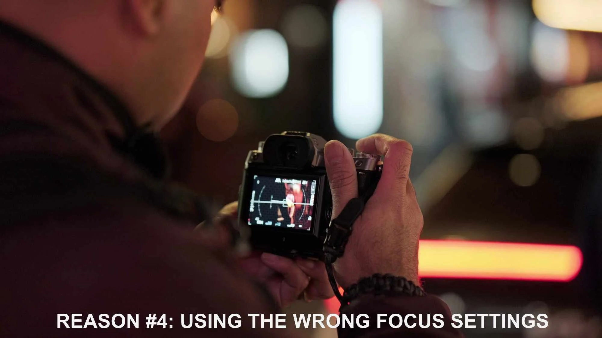 Photographer reviewing a camera screen in a dimly lit setting, with blurred lights in the background.