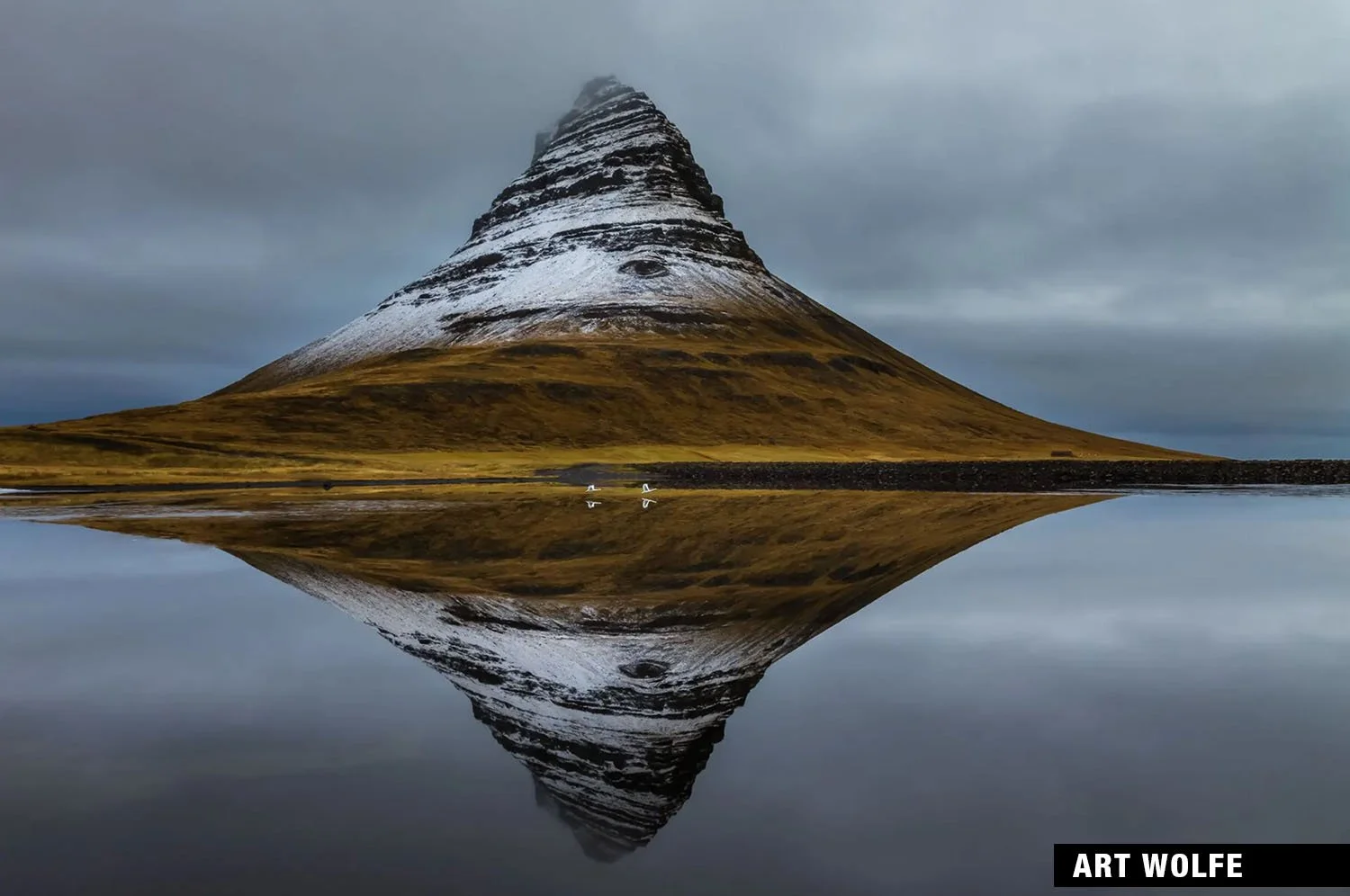 Kirkjufell mountain in Iceland, reflected in water under a cloudy sky by Art Wolfe