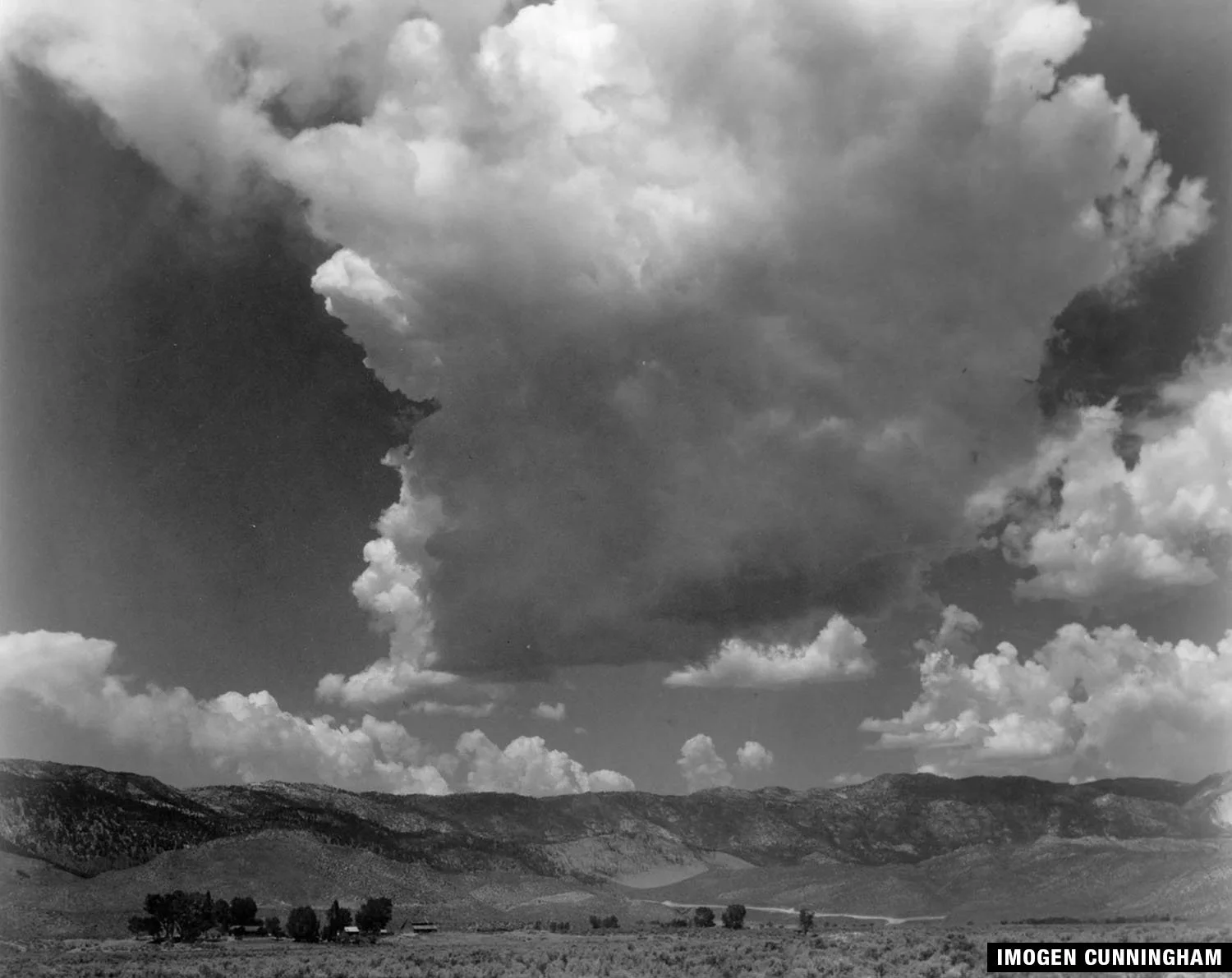 A black and white photo of dramatic clouds towering over a mountainous landscape.