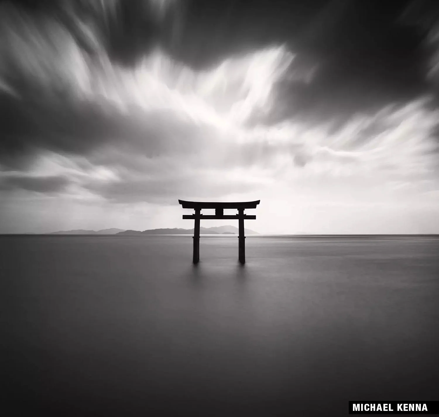 Black and white photo by Michael Kenna: lone torii gate in water under dramatic sky.
