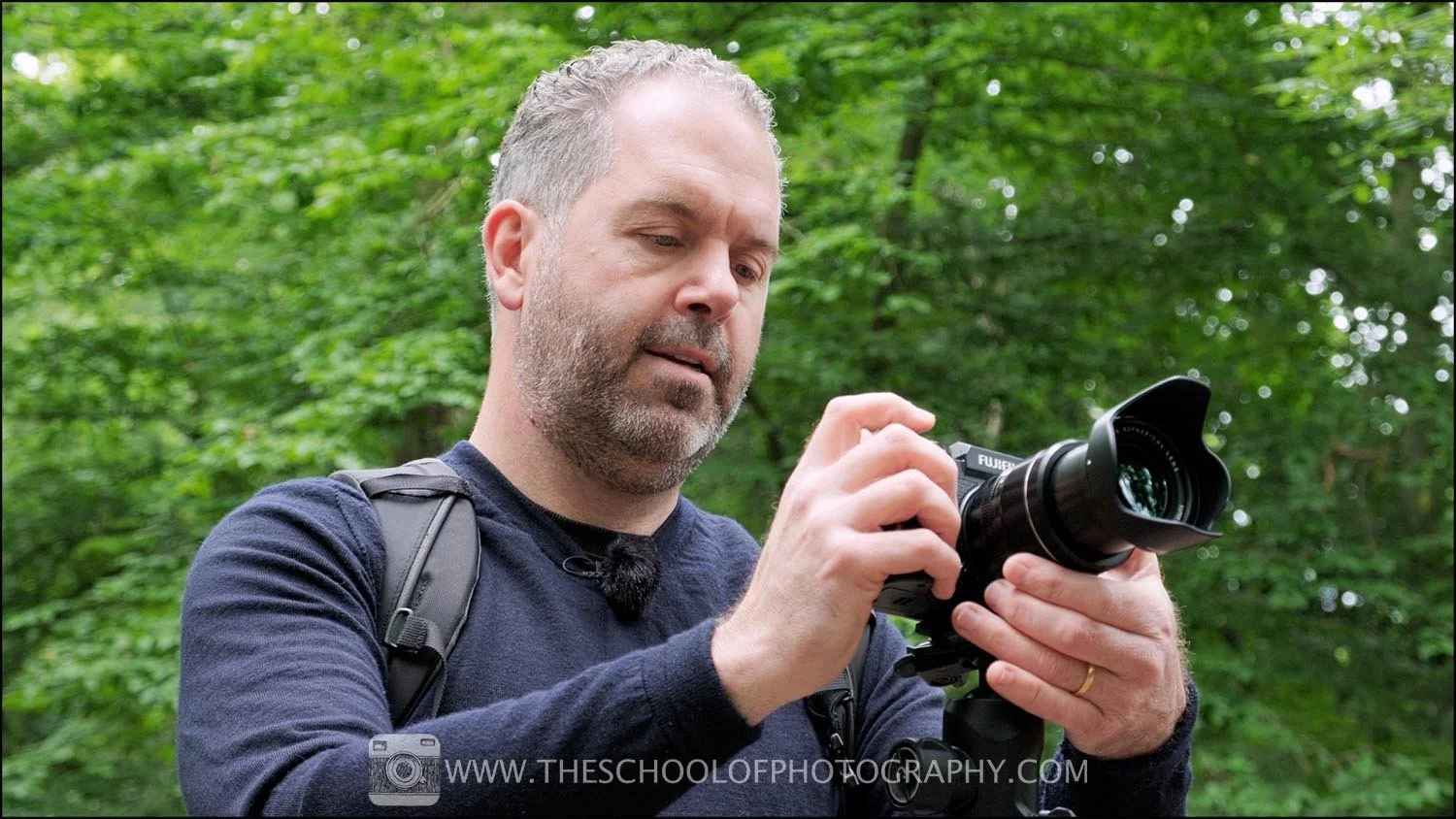 Videographer adjusting camera settings while filming outdoors in a forest, demonstrating hands-on camera operation and movement techniques.