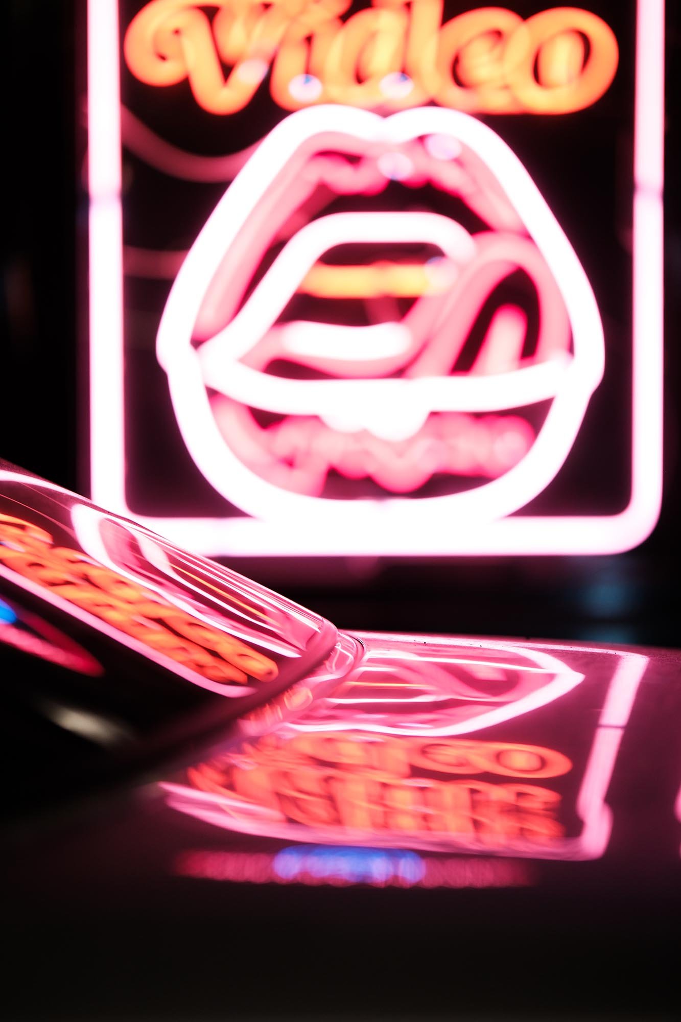 Neon lips sign reflected on a car window in a colourful urban street photography scene