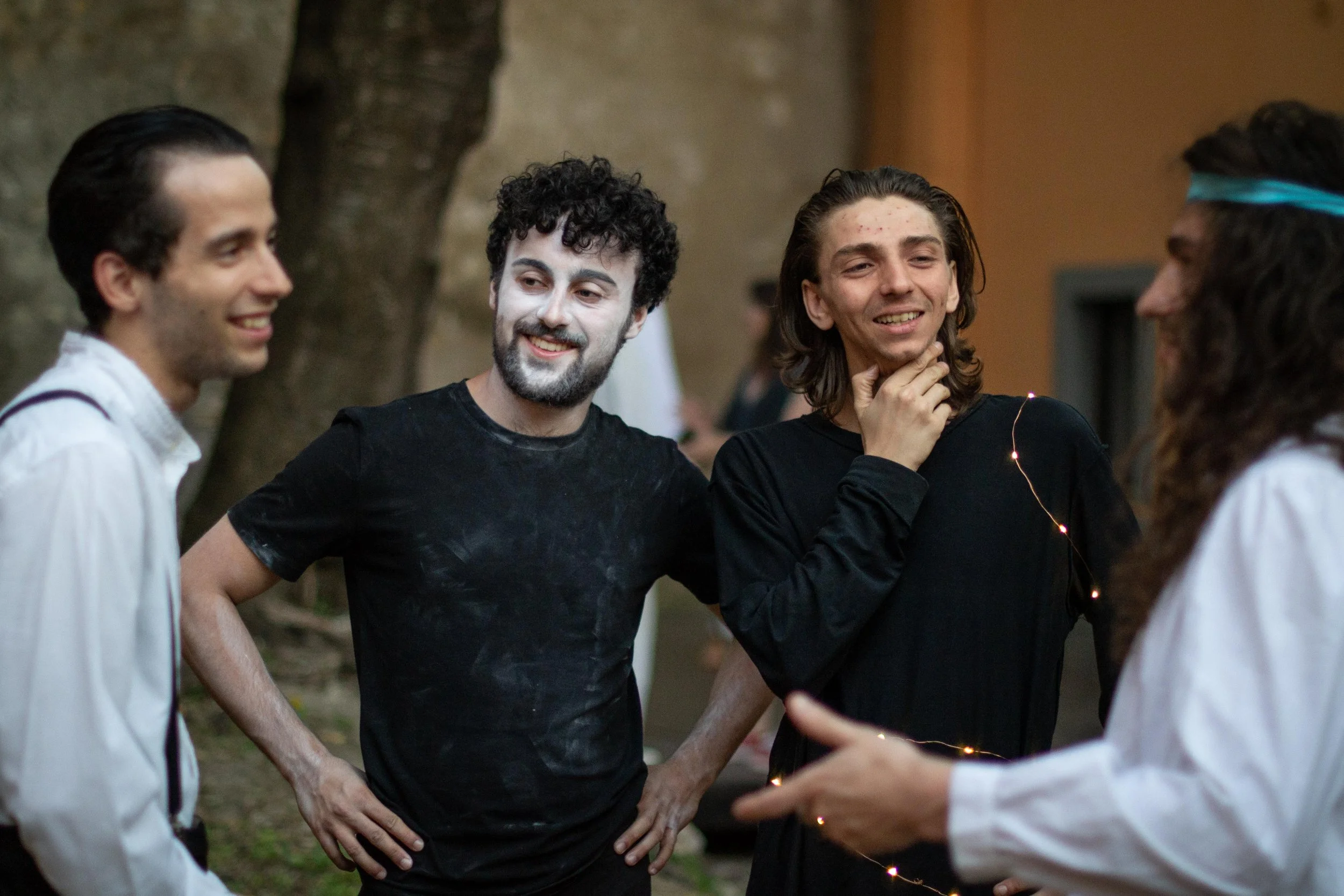 Quattro persone sorridenti e rilassate stanno conversando all'aperto, con due di loro vestiti in abbigliamento da festa o costume, mentre condividono un momento di socializzazione.