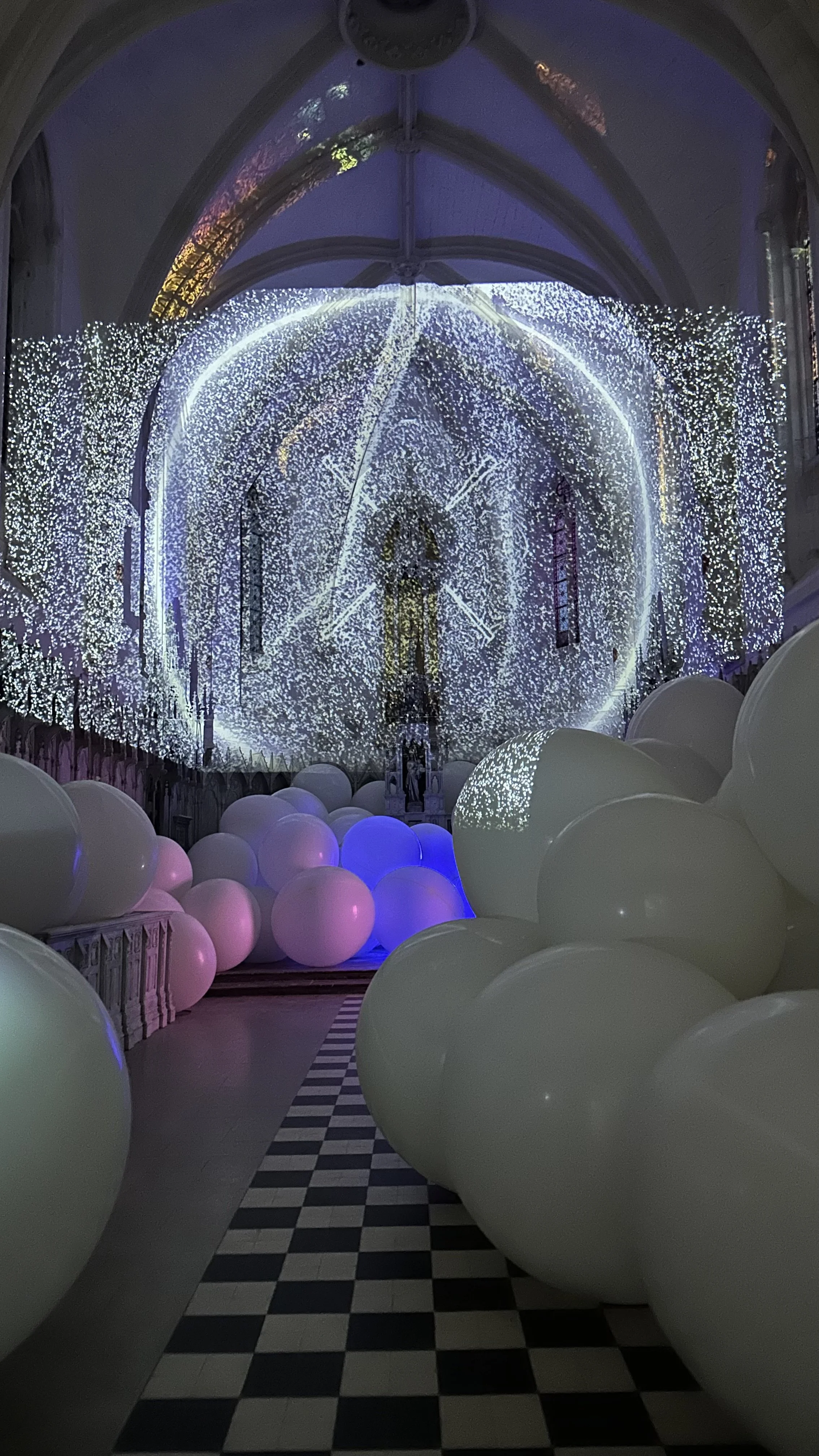 Interno di una chiesa decorato con luci natalizie e palloncini bianchi, con una strada a scacchi al centro.