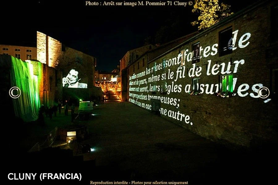 Proiezione di un testo in francese e un'immagine di un uomo sulla parete di un edificio a Cluny, Francia, durante la notte.
