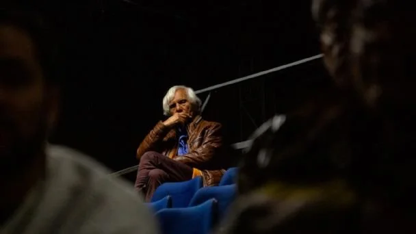 Uomo anziano con capelli bianchi seduto, che si morde un dito in un ambiente al chiuso