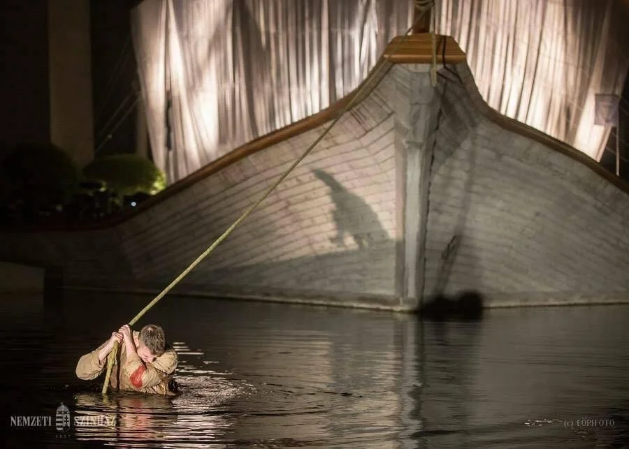 Due persone che si abbracciano in acqua davanti a una grande imbarcazione storica, probabilmente un' nave antica, di notte.