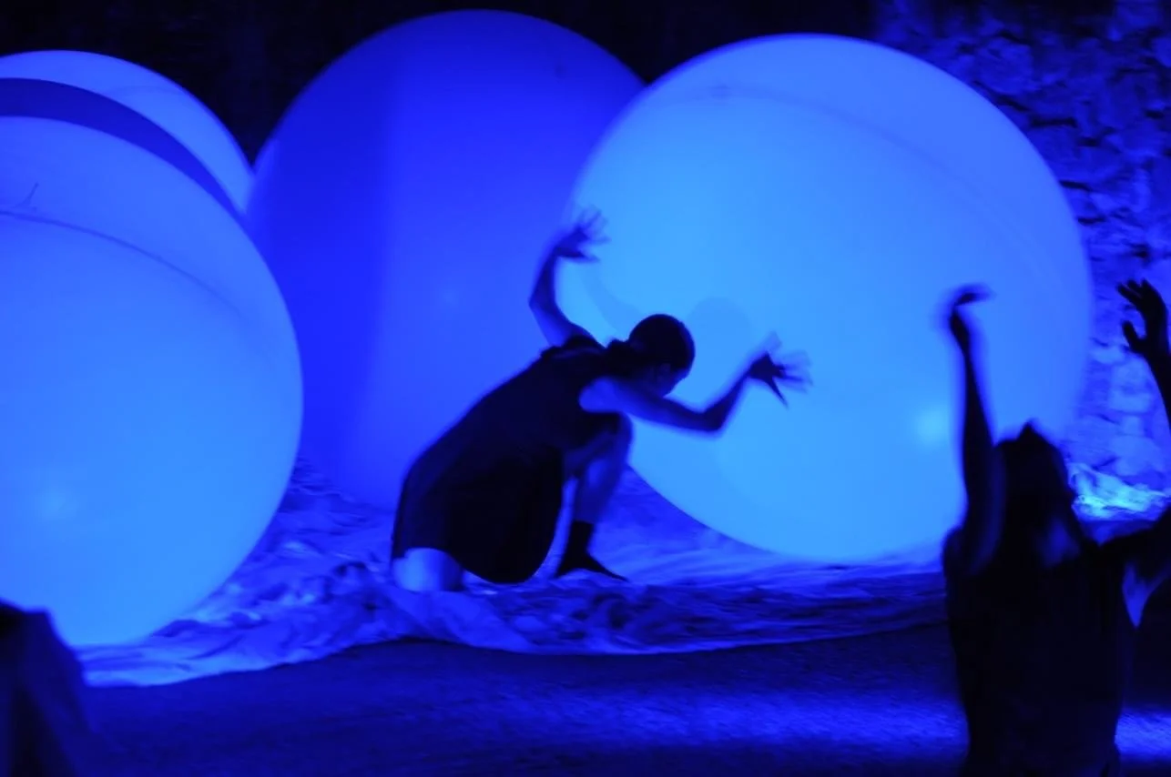 Danza con luci blu di due persone su un palco con grandi sfere luminose.