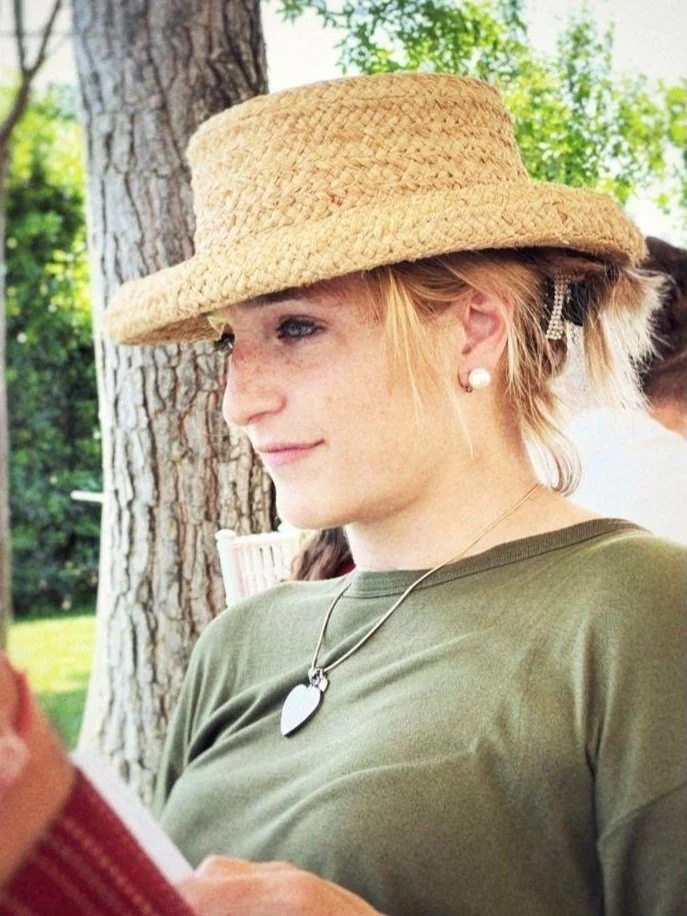 Una donna con cappello di paglia che legge un libro all'aperto, in un parco.