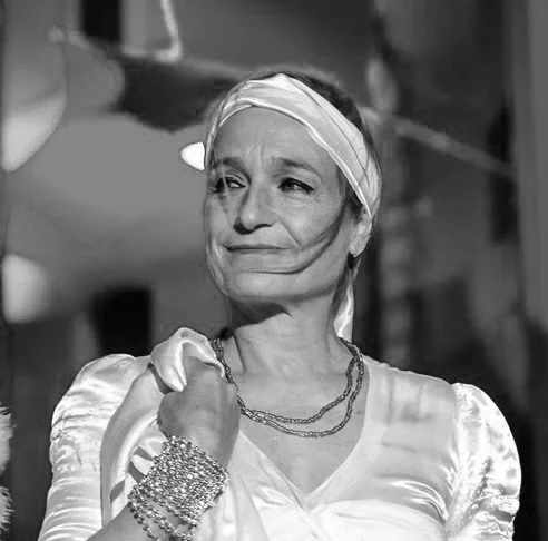 Una donna anziana con un turbante in testa, indossa gioielli e un vestito lucido, sembra un personaggio di un film in bianco e nero.