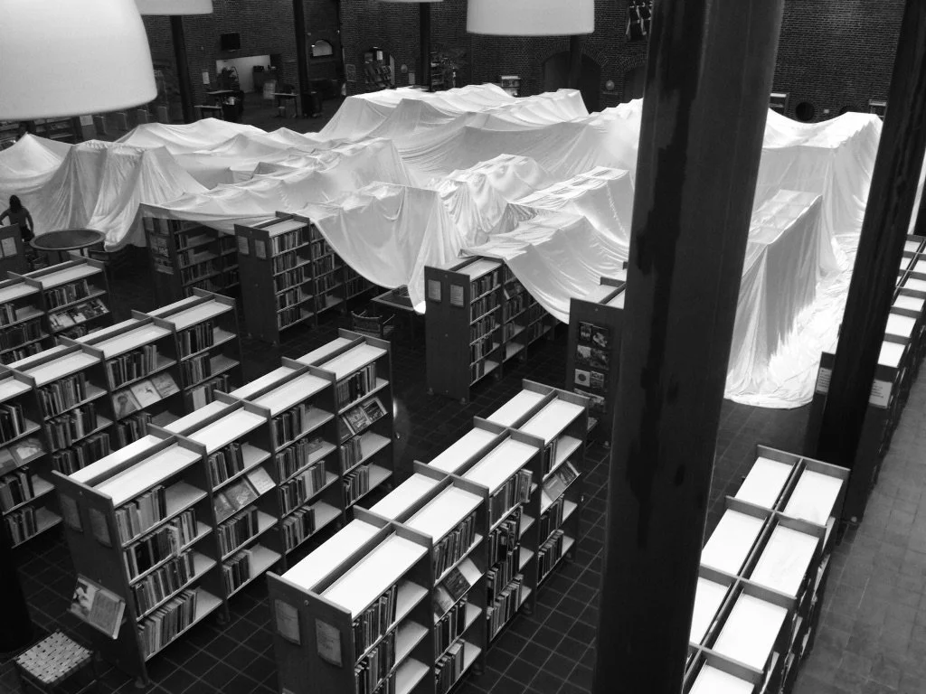 Scaffalature di libri in una biblioteca con tende bianche che coprono alcune aree