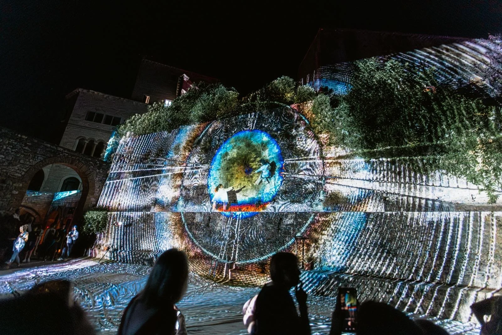 Lo spettacolo di luci e proiezioni su un edificio storico con persone che osservano e fotografano l'evento di notte.