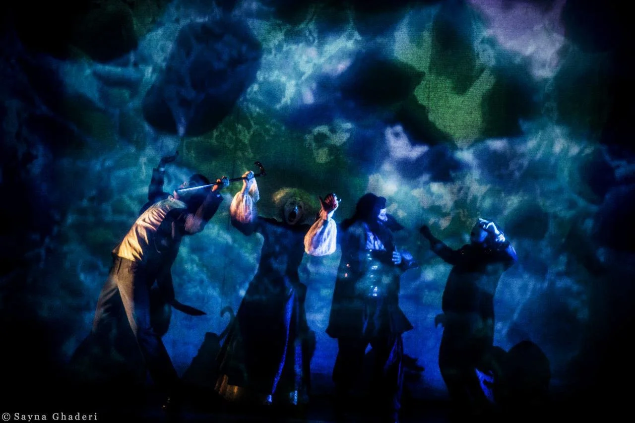 Performers in costume during a theatrical show with colorful background projection.