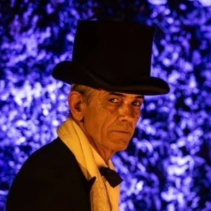 Un uomo vestito in stile formale con cappello a cilindro, sfondo bluastro artistico.