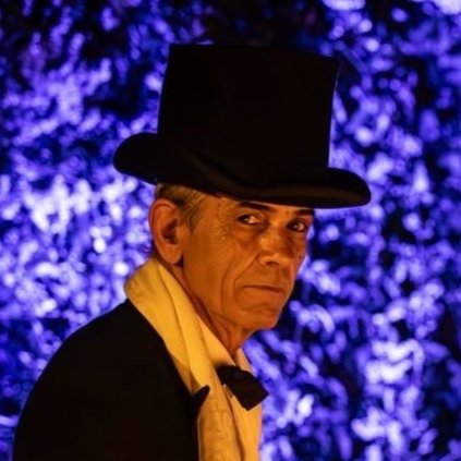 Un uomo vestito in stile formale con cappello a cilindro, sfondo bluastro artistico.