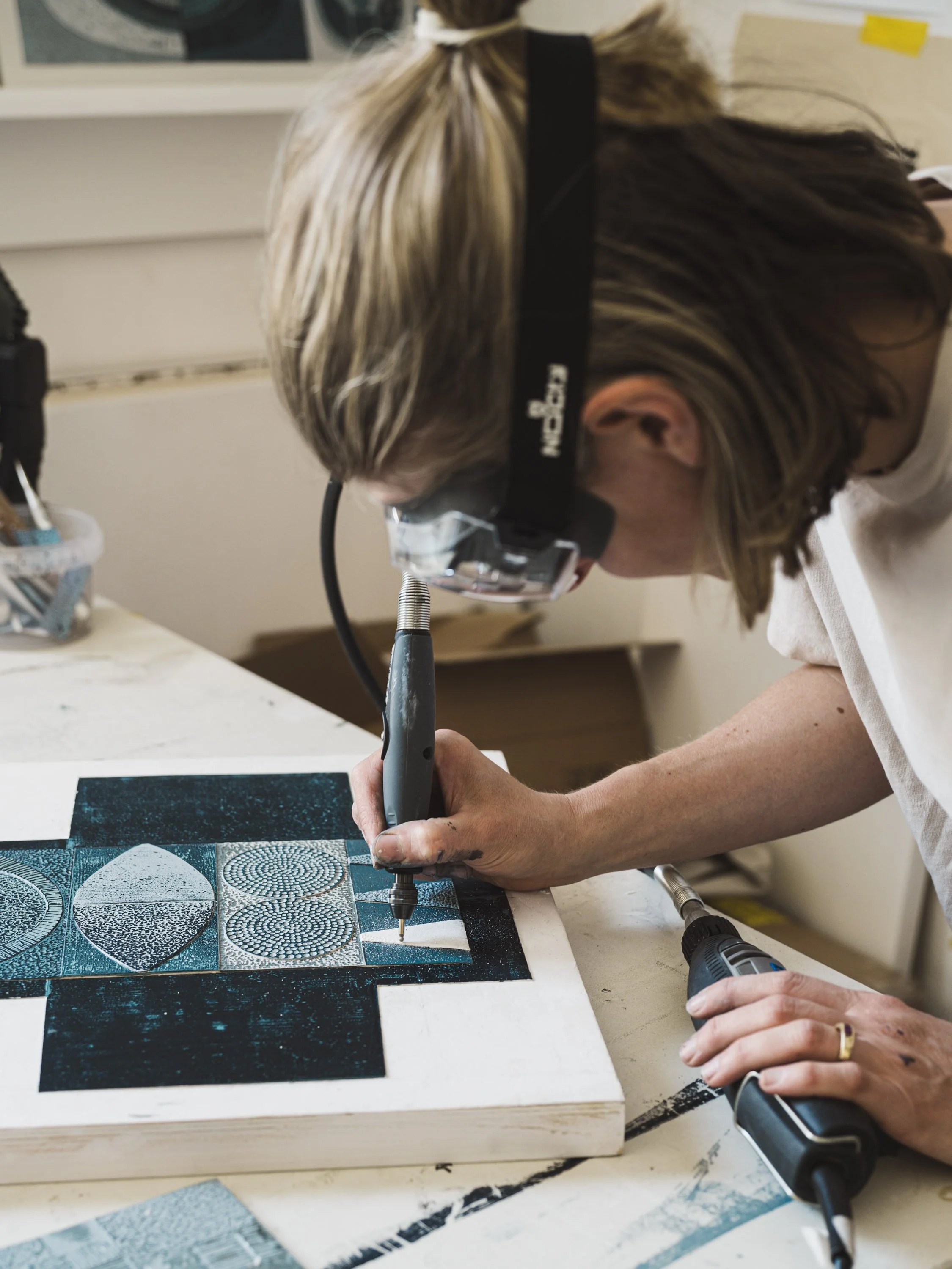 Person using a handheld rotary tool to work on a piece of artwork or material with a detailed, patterned surface.