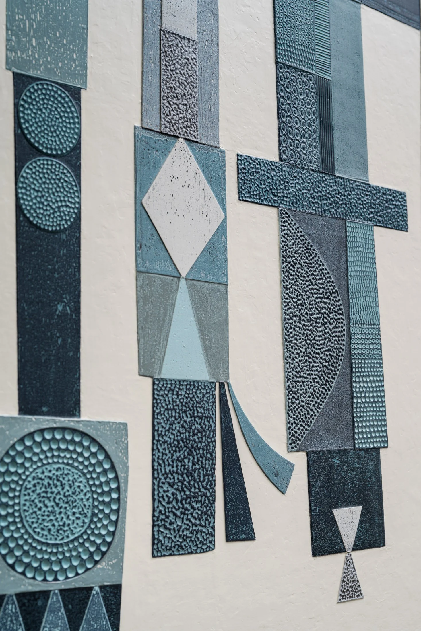 Textured blue and gray geometric wall art with various patterns including circles, lines, and dots, arranged in rectangular and diamond shapes.