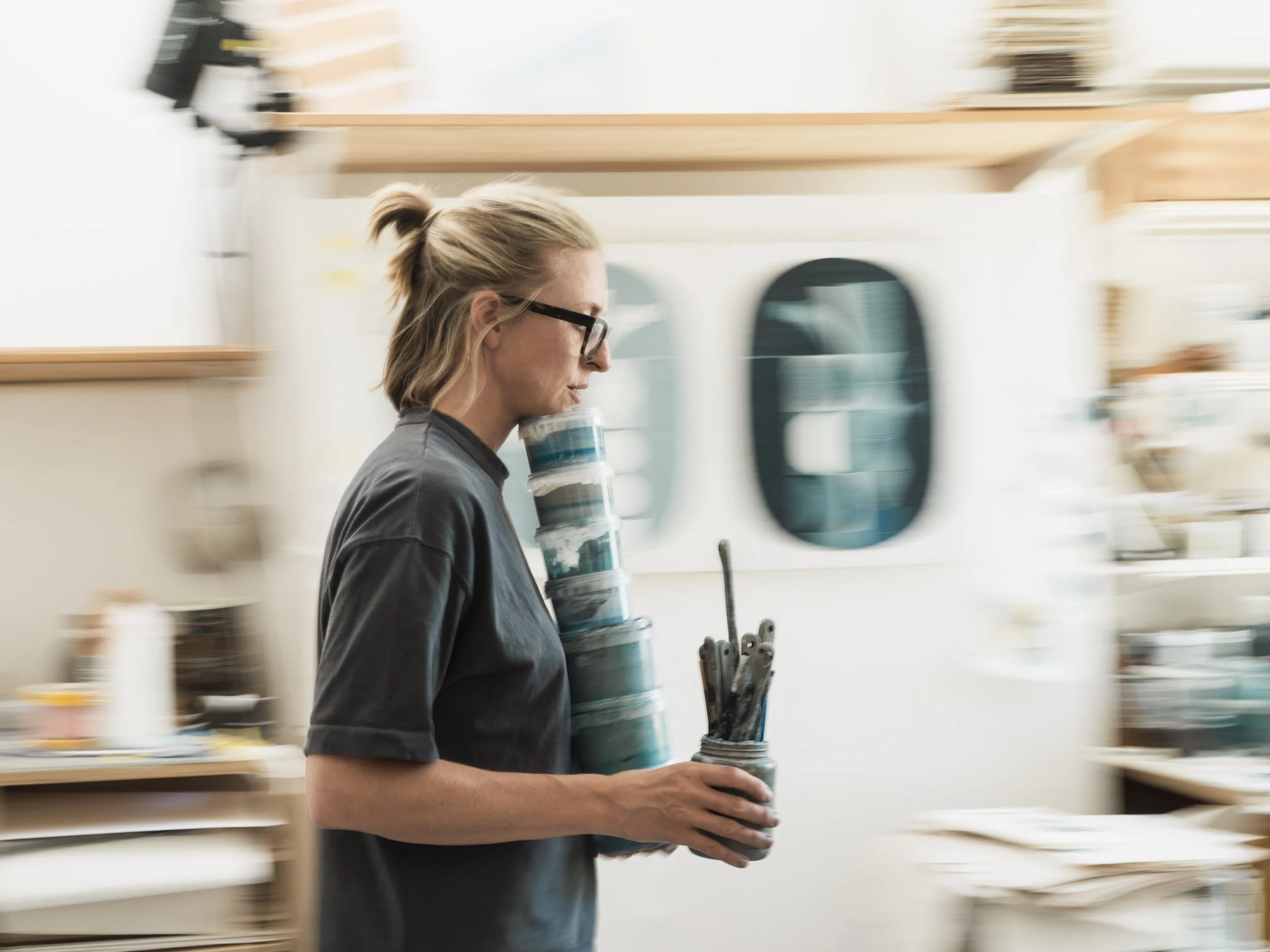 Sanna Annukka carries a pot of paint brushes in her studio