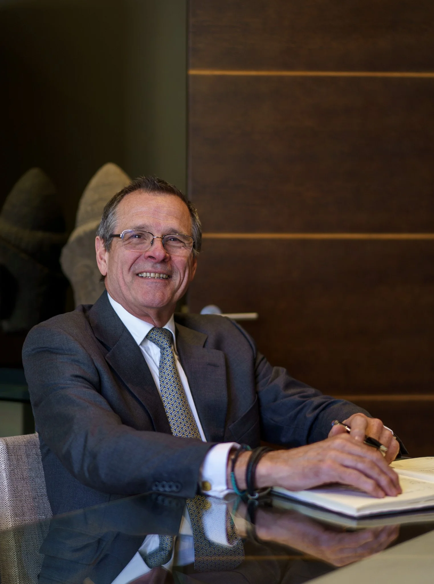 Smiling man in a suit sitting at a table with a notebook, brown panel background.
