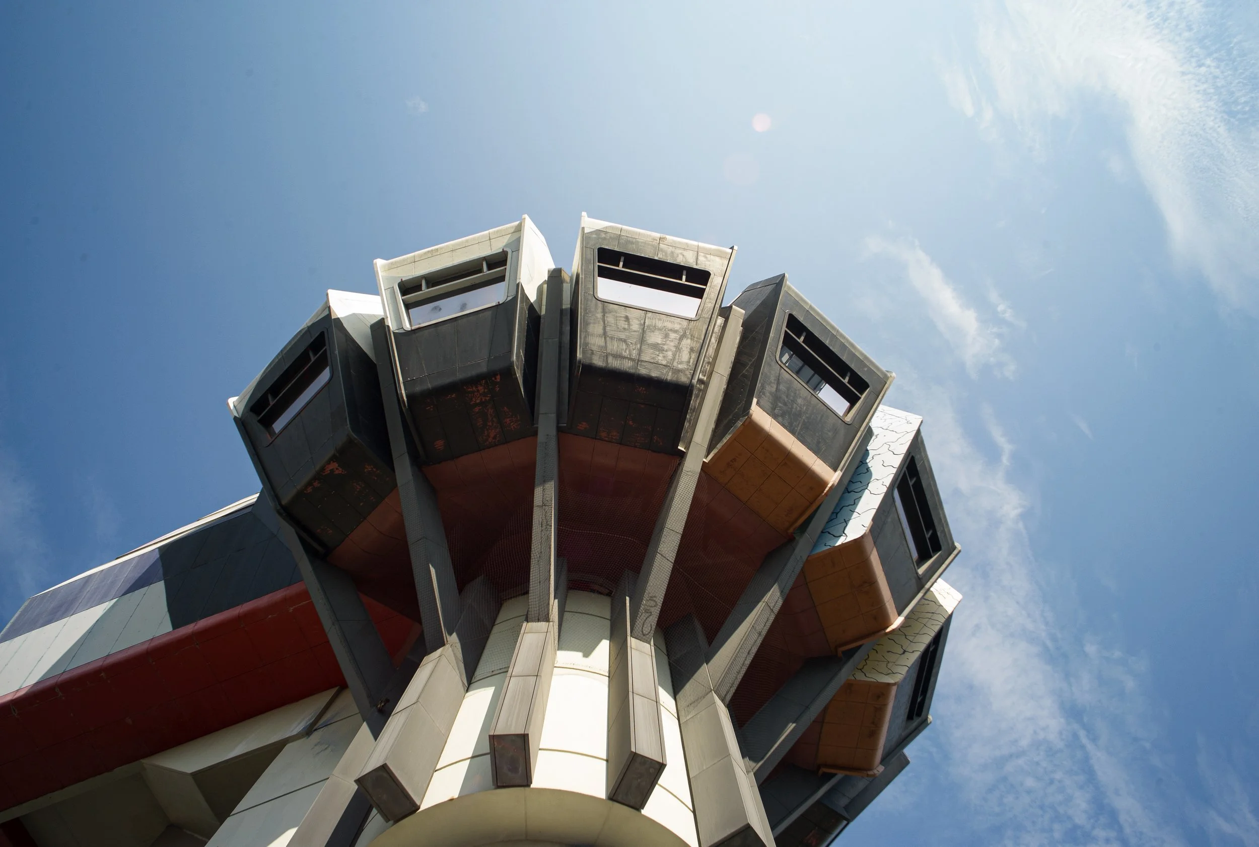 Looking up at a futuristic building or structure with angular, metallic panels against a bright blue sky with some wispy clouds.