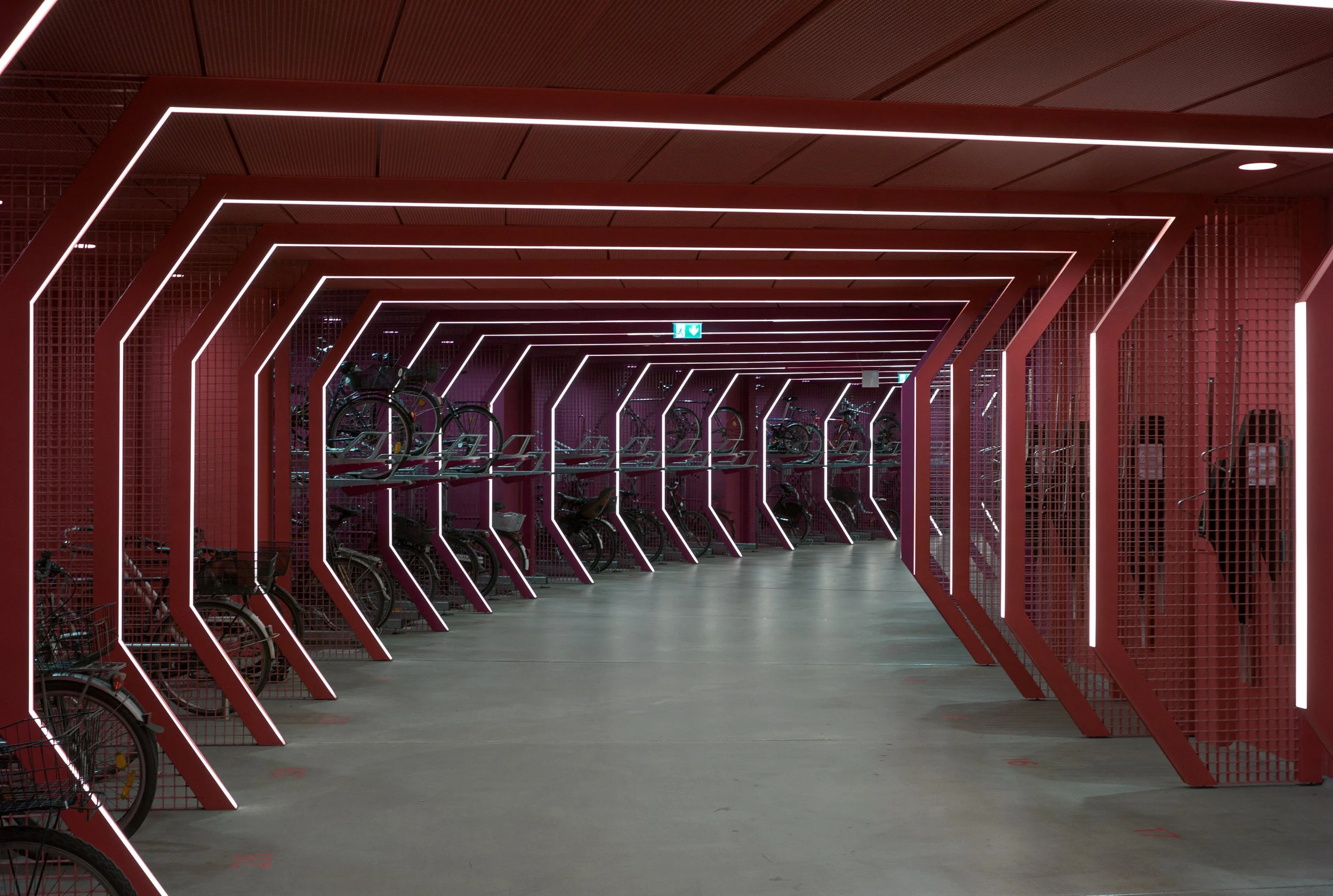 Indoor bike parking area with red metal bike racks and neon lighting accents.