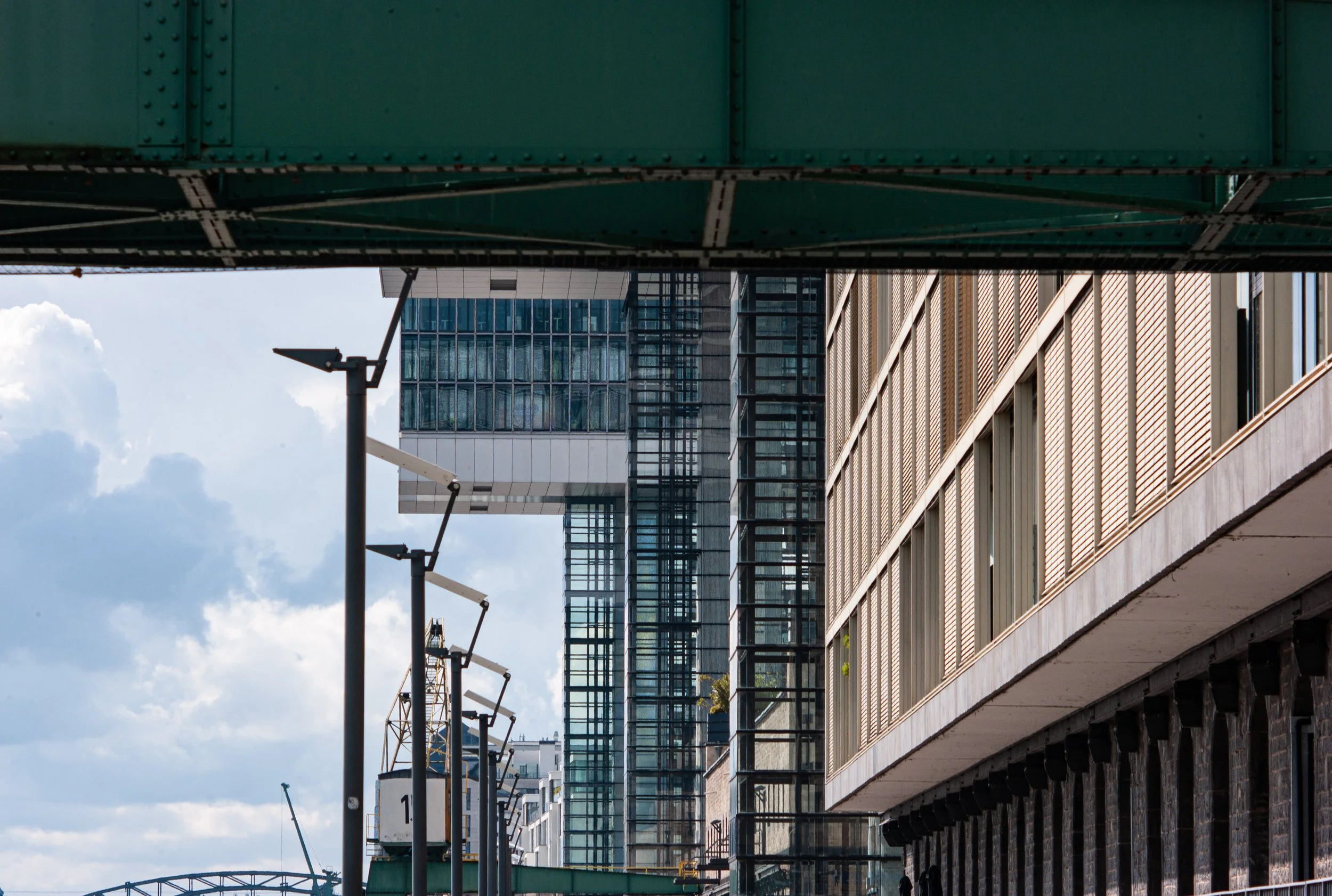 Cityscape featuring modern high-rise buildings with glass windows, partly under an overpass structure, with a cloudy sky in the background.