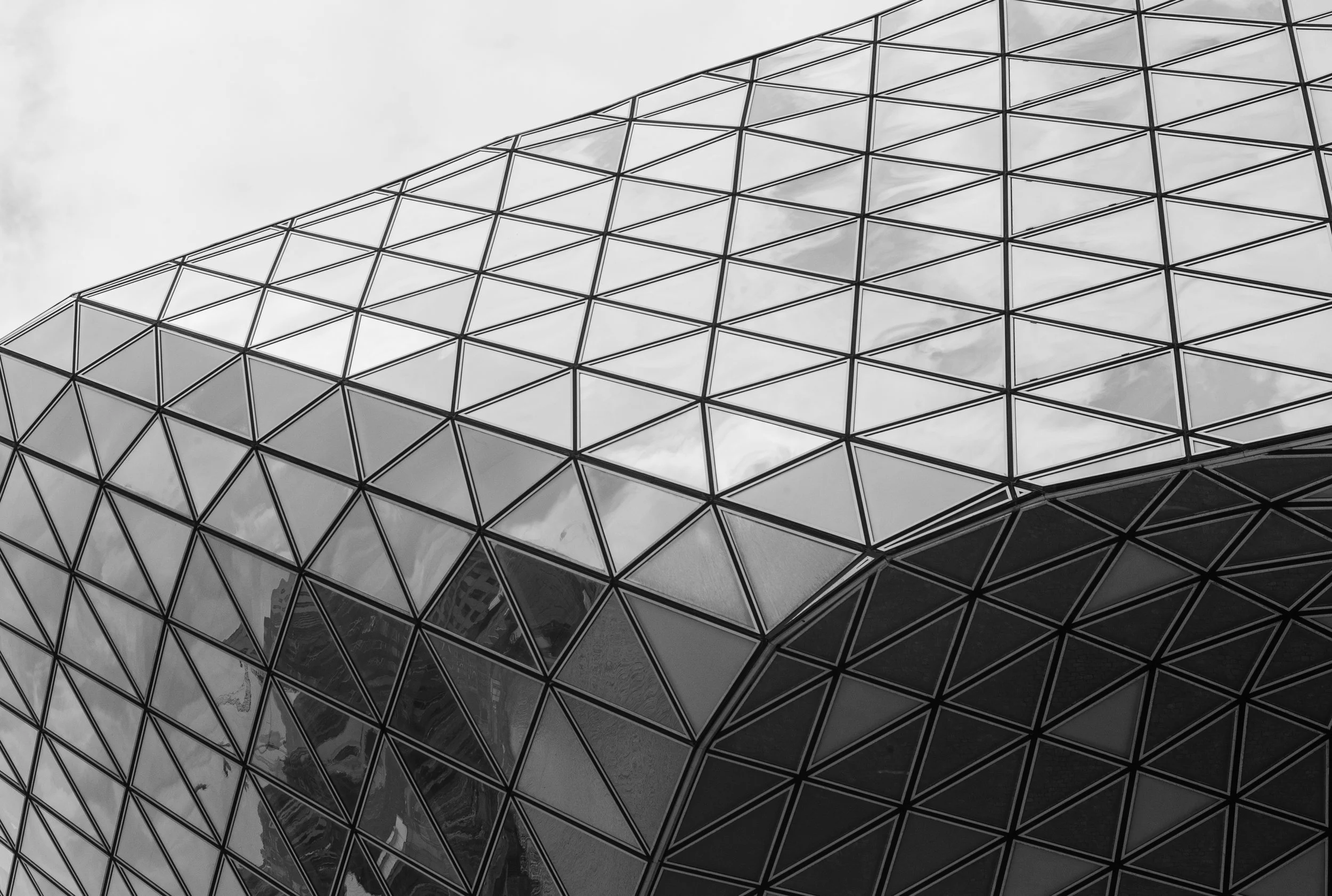 Close-up of a modern building with a geometric glass facade in black and white, showing triangular and diamond-shaped patterns.