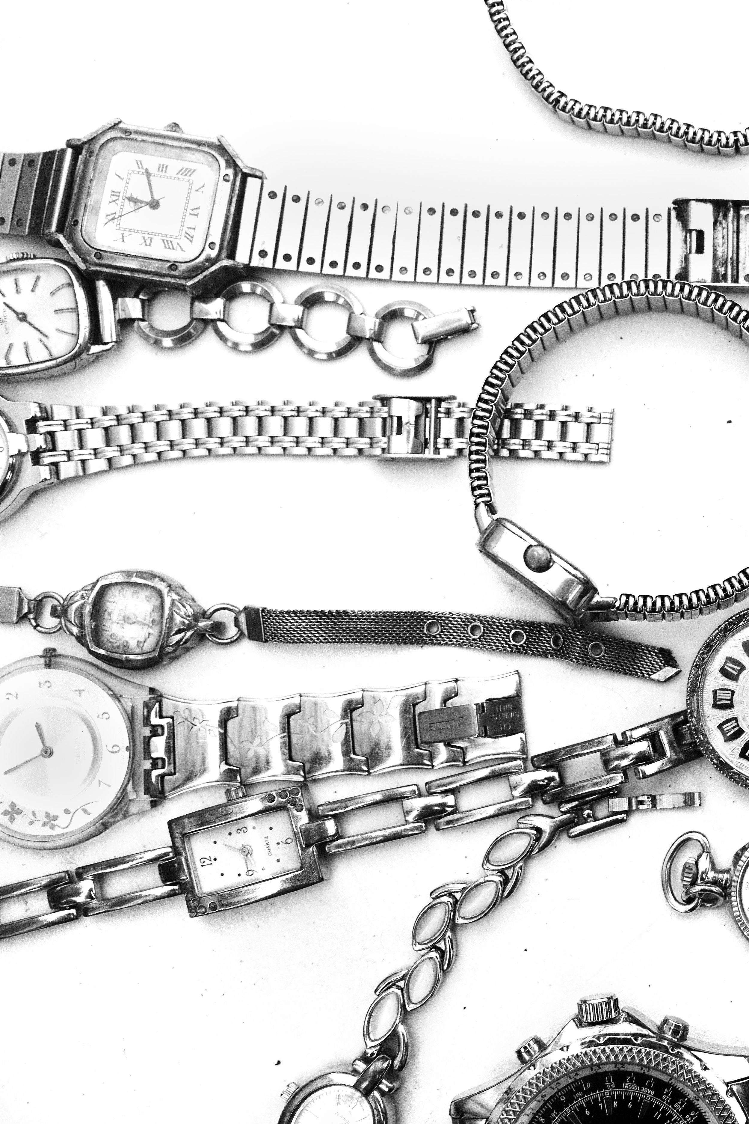 Schwarz-weiß-Fotografie verschiedener Armbanduhren und Schmuckstücke auf einem weißen Hintergrund.