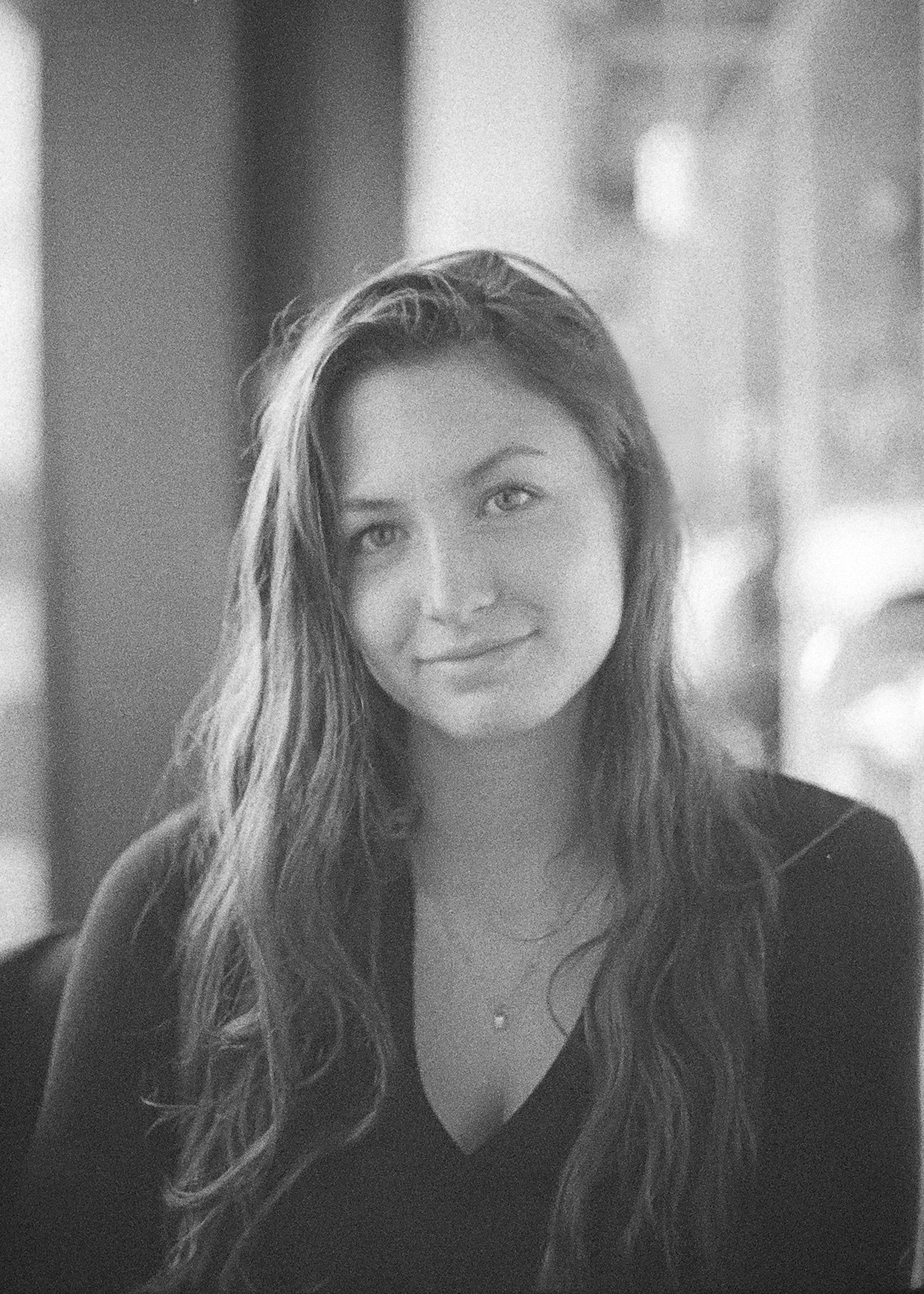 Schwarz-weiß-Foto einer jungen Frau mit langen, gewellten Haaren, die leicht lächelt.