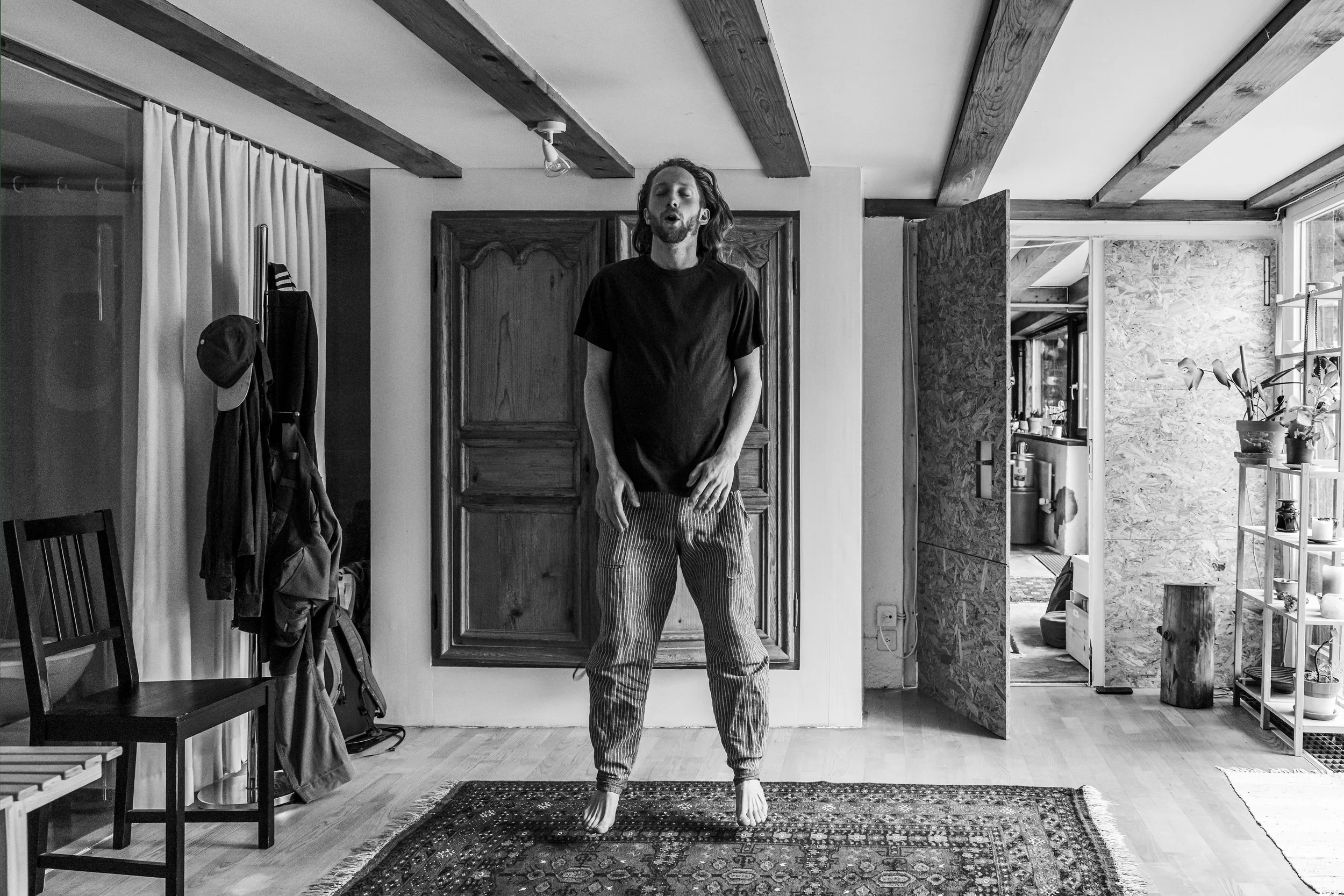 Mann steht barfuß auf einem Teppich in einem Zimmer, das innen mit Holz und Steinelementen dekoriert ist.