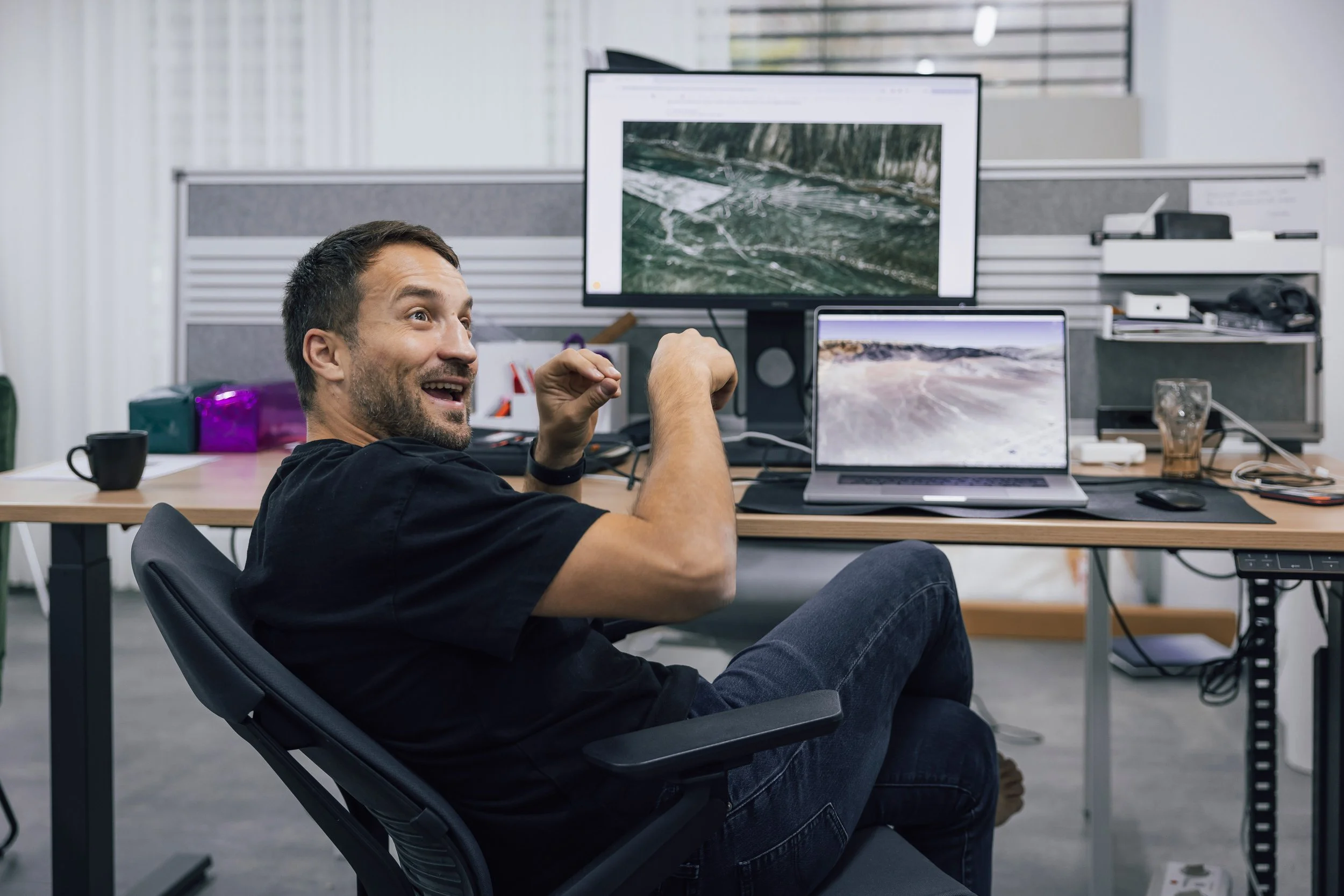 Mann sitzt an einem Schreibtisch mit zwei Monitoren, lachen und freut sich in einem Büro