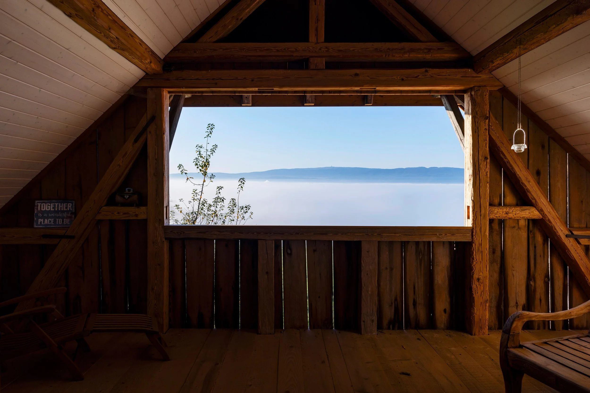 Innenraum eines Baumhauses mit Blick auf einen See und Berge, Holzverkleidung, kleine Dekorationen und ein Schild mit dem Text 'TOGETHER is a wonderful PLACE TO BE'