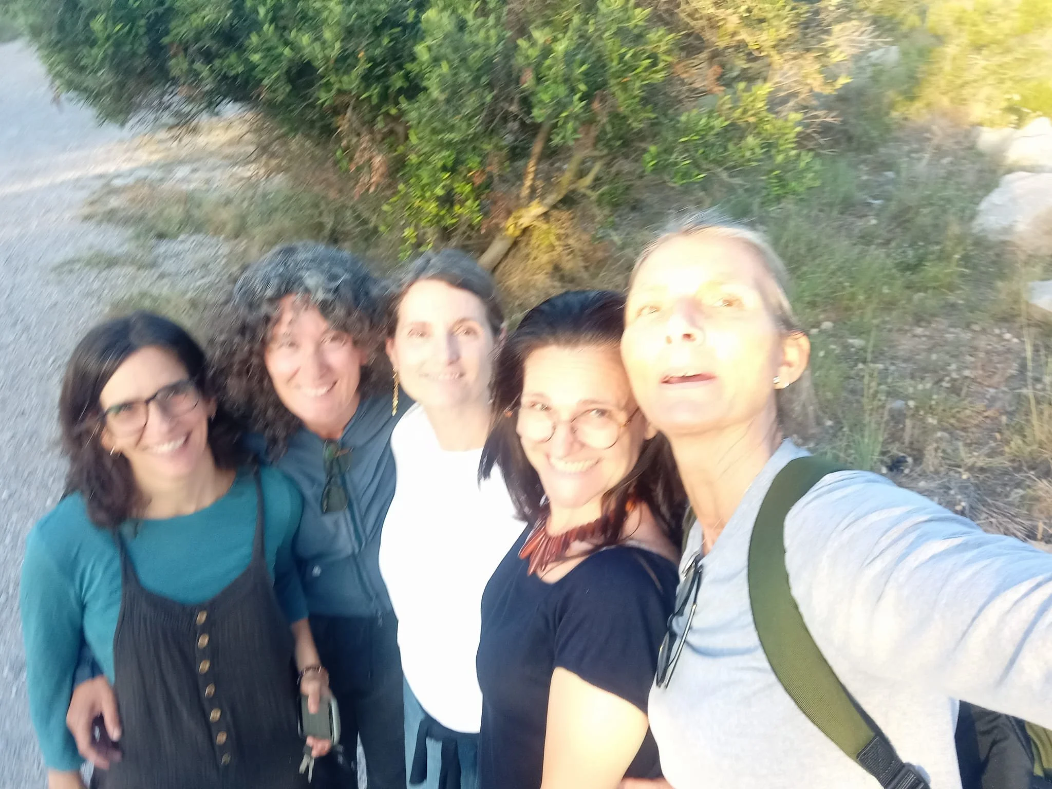 Incorpore Natura. Baños de bosque. Forest Bath. Group of five smiling women taking a selfie outdoors on a sunny day, standing on a path next to greenery.