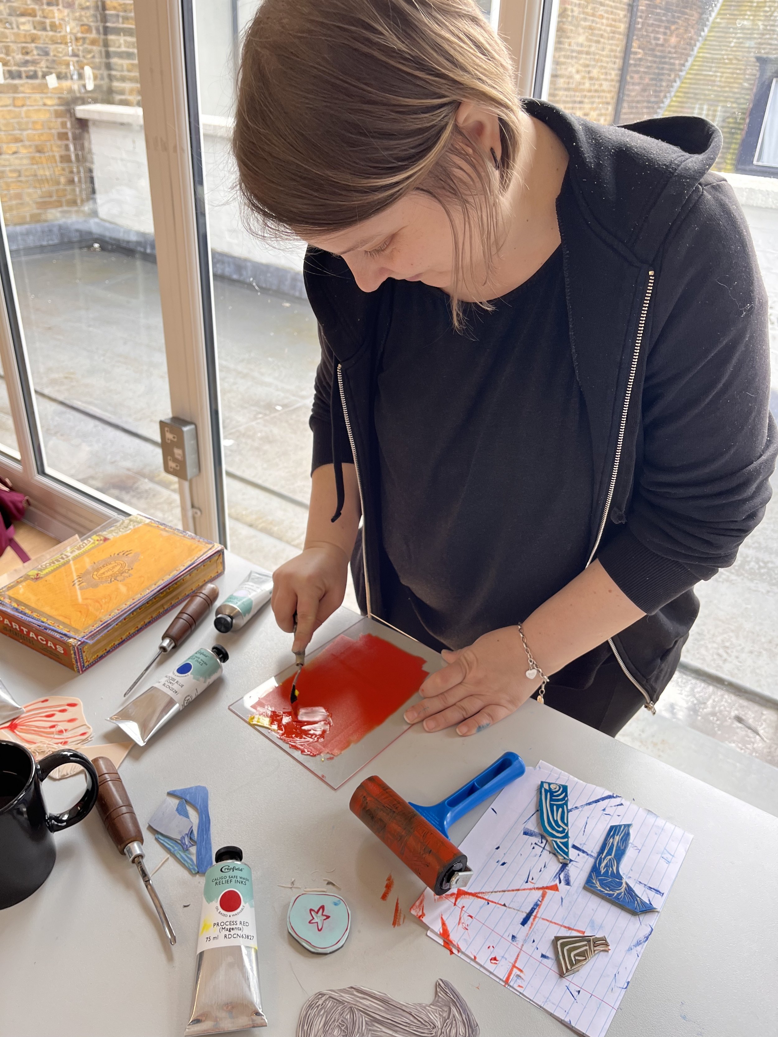 Person engaged in printmaking process at a table with inks and tools.