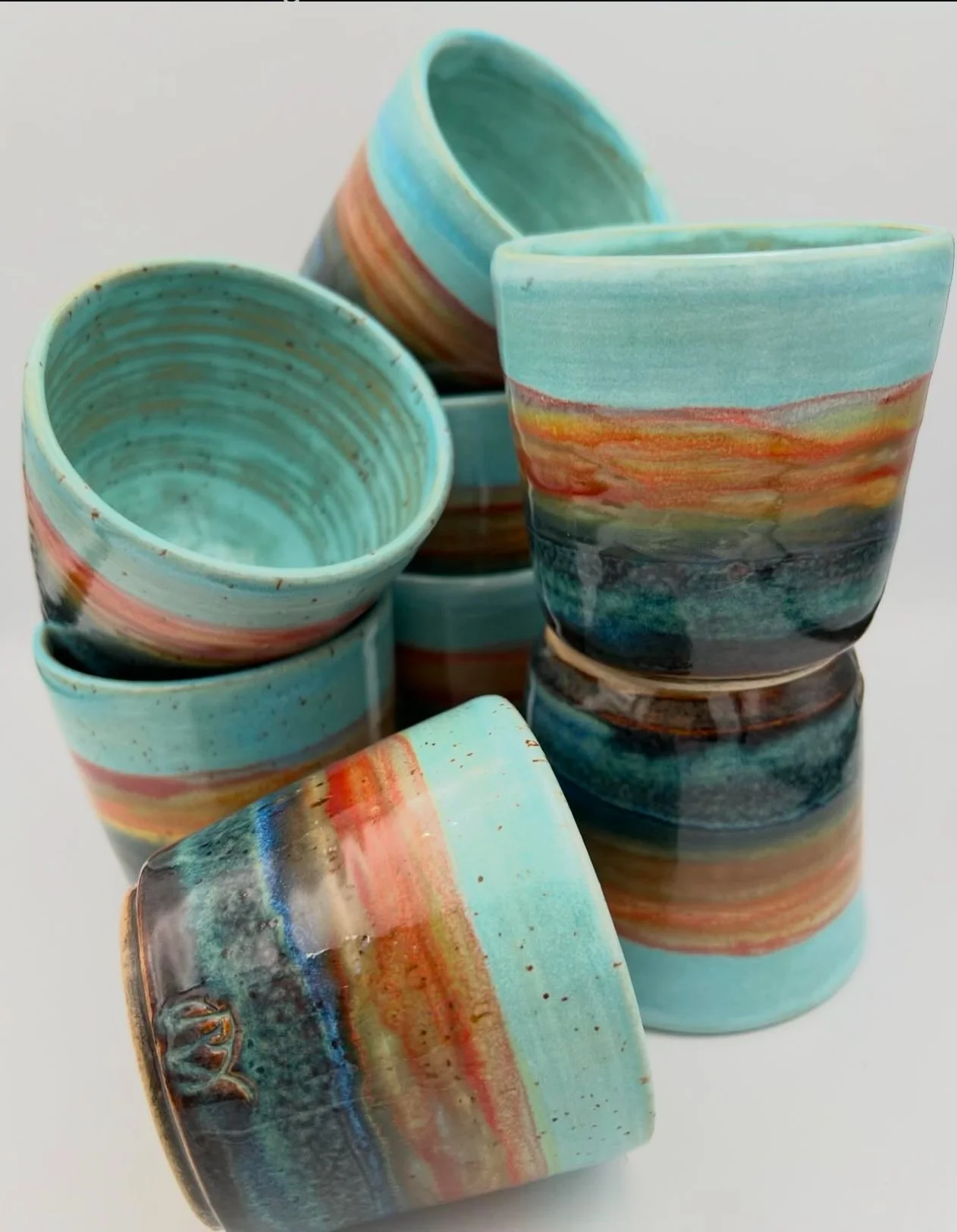 Een stapel kleurrijke keramieken bekers met een aardse, gemengde tinten in een abstracte patroon.