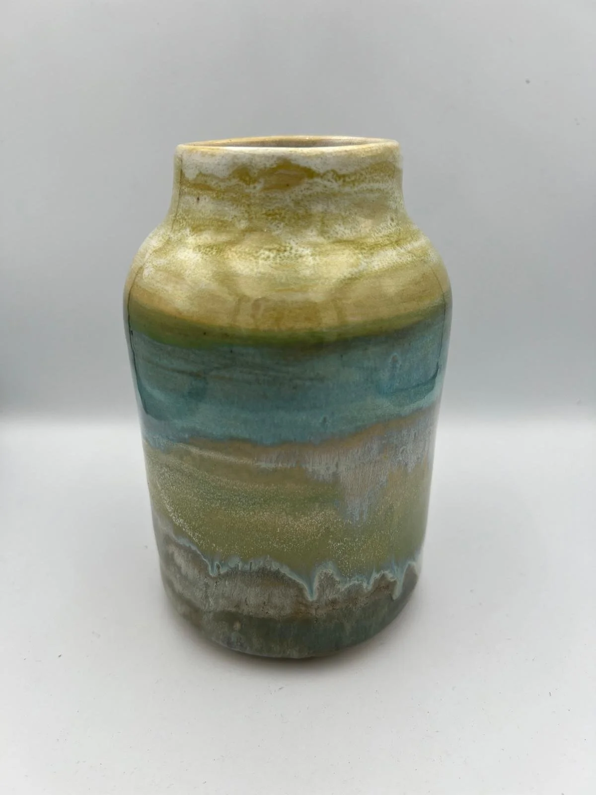 Een keramieken vaas met een gemarmerde glazuur in tinten geel, groen, blauw en bruin, afgebeeld op een witte achtergrond.