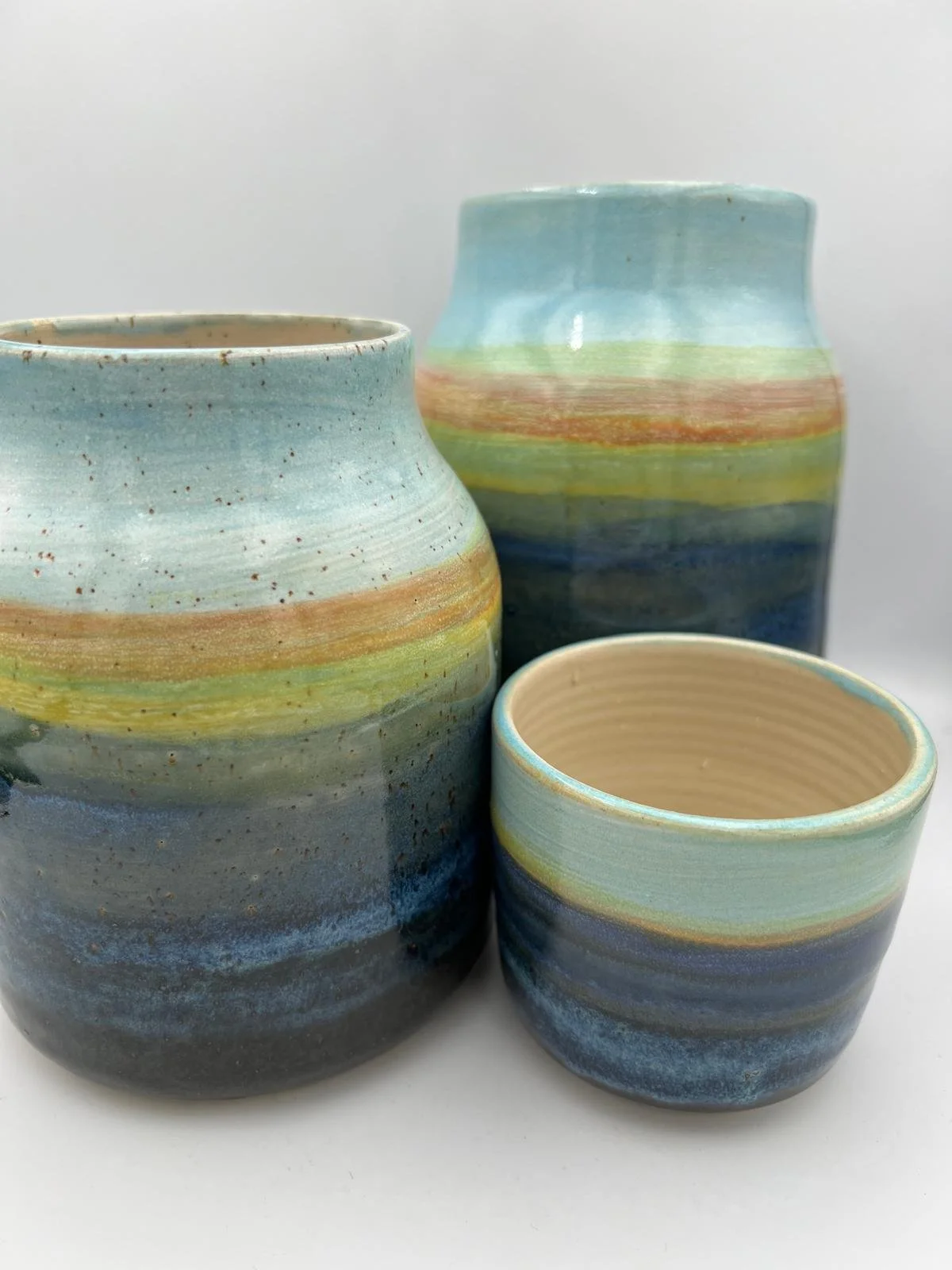 Drie kleurrijke, handgemaakte keramische vazen en een kopje met een abstract, strepenpatroon in pastelkleuren.