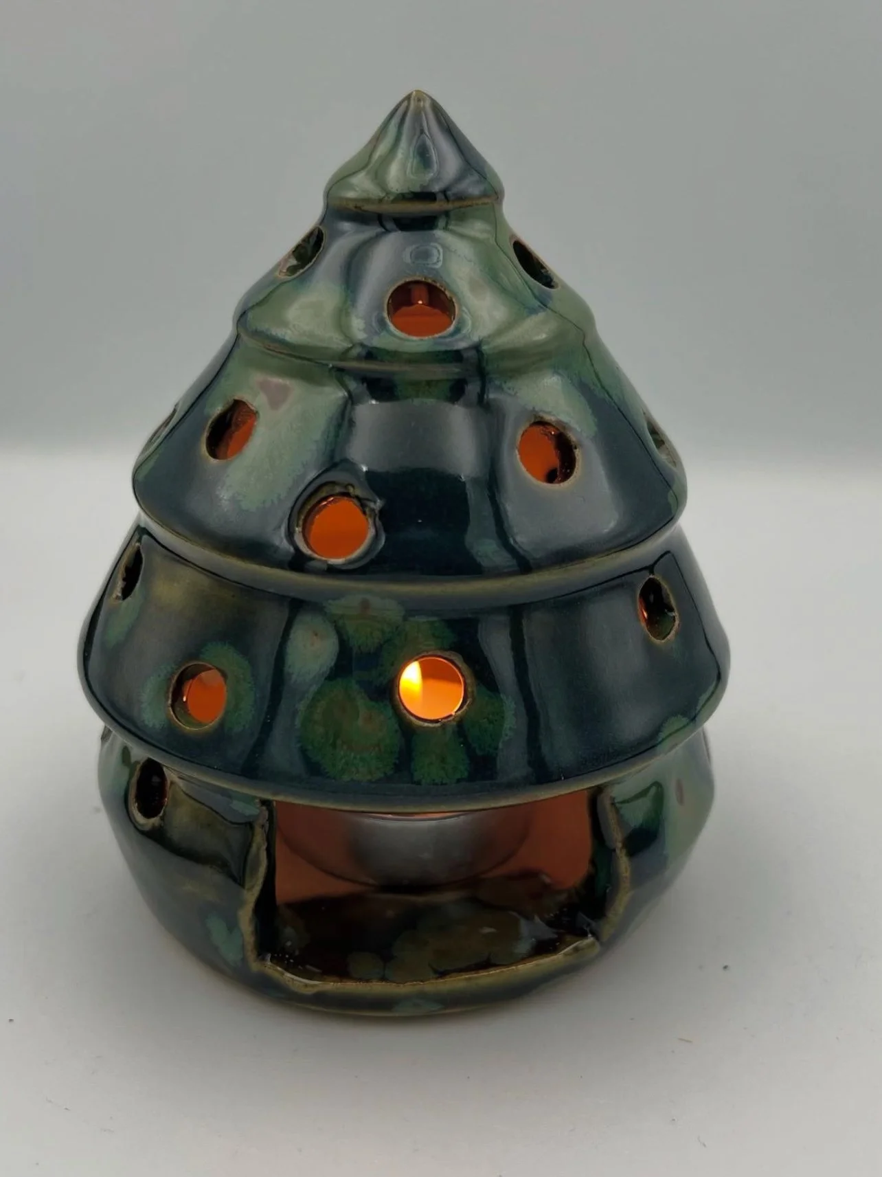 Gekleurde keramieken waxinelicht houder in de vorm van een kerstboom met openingen voor het licht.