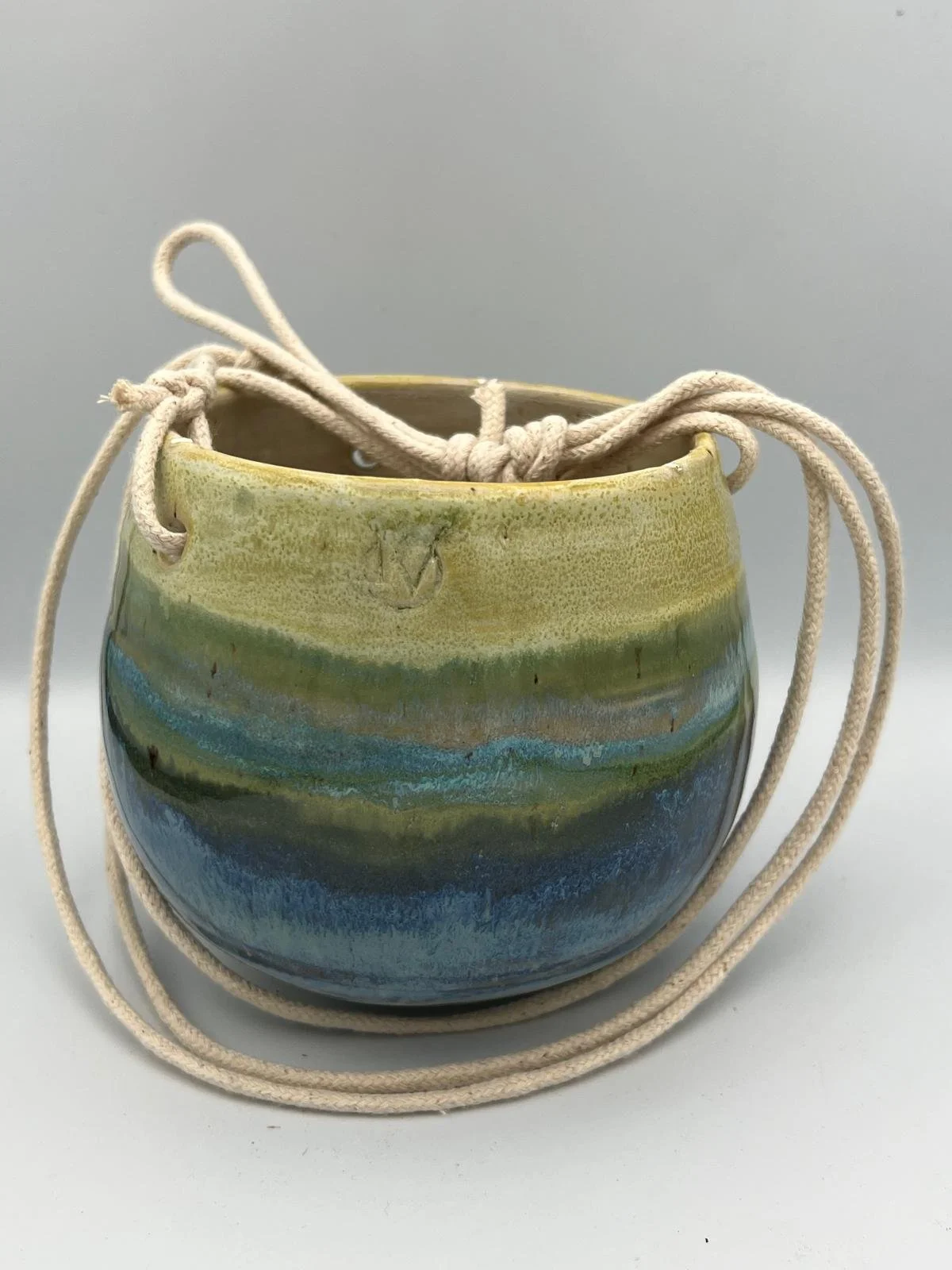 Kleine ronde keramieken pot met groene, blauwe en beige glazuur, met een beige touw eromheen.