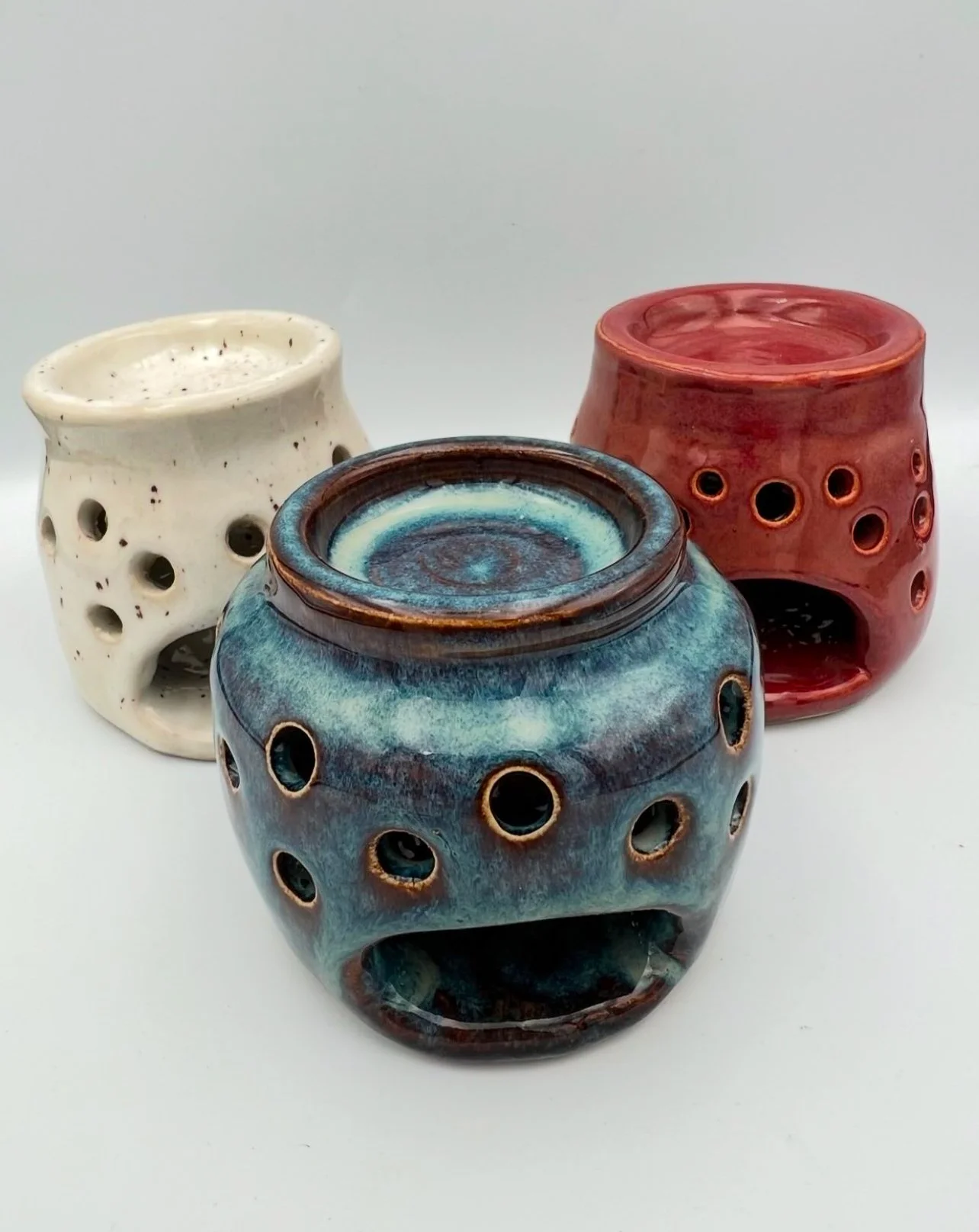 Drie gekleurde keramische geurbranders met gaten, in wit, blauw en rood.