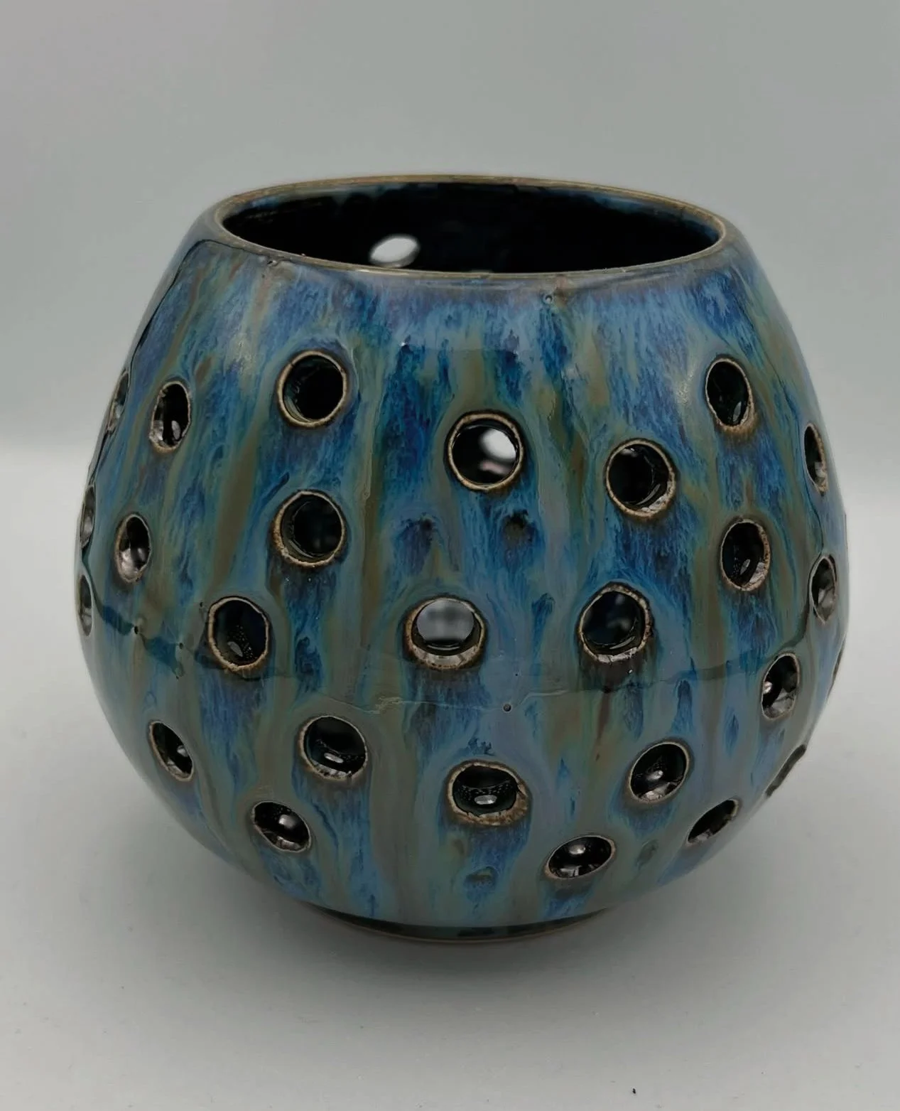 Een ronde, blauw-groen gekleurde keramische vaas met meerdere openingen rondom, geplaatst op een witte achtergrond.