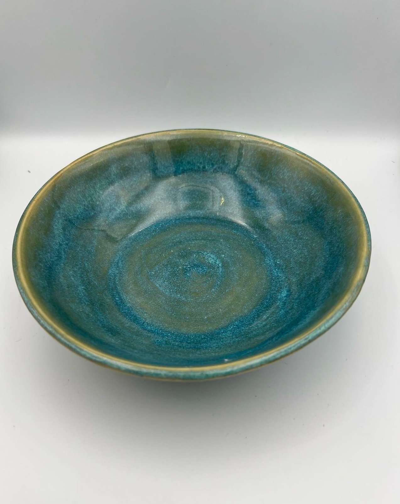 Een ovale keramieken kom met een blauwe en groene glazuurlaag, geplaatst op een witte achtergrond.