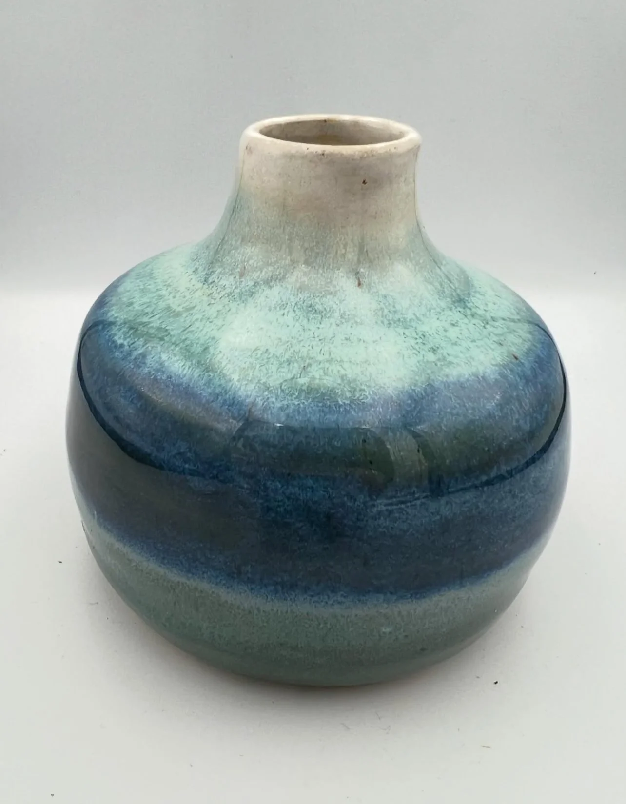 Een keramische vaas met een ronde, bolvormige body en een korte smalle hals, versierd met blauwe en groene glazuurverf.