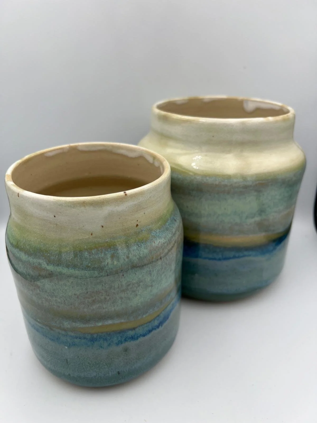 Twee keramieken potten met glaze in pastelkleuren, gevuld met een vloeistof.