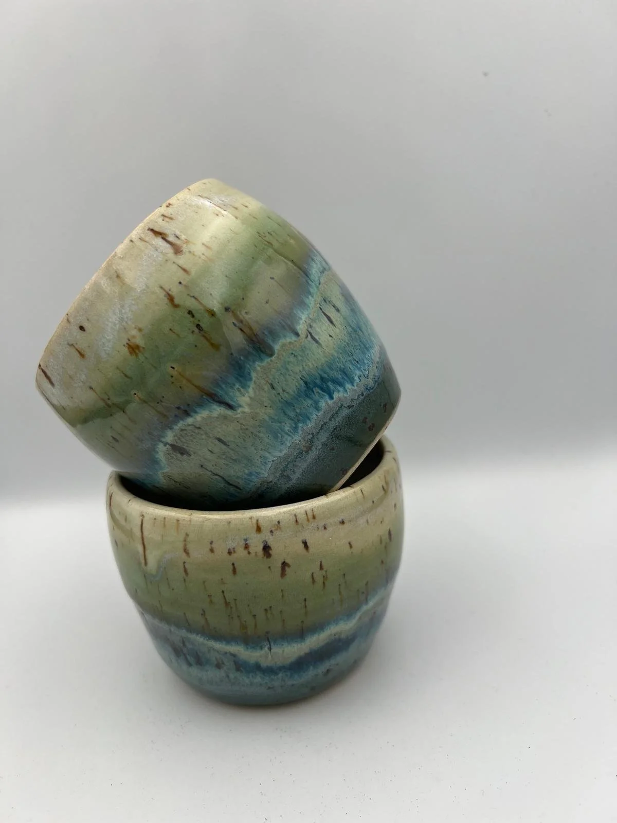 Twee gegroefde keramische potten met blauwe en groene strepen, een bovenop en de andere onder.