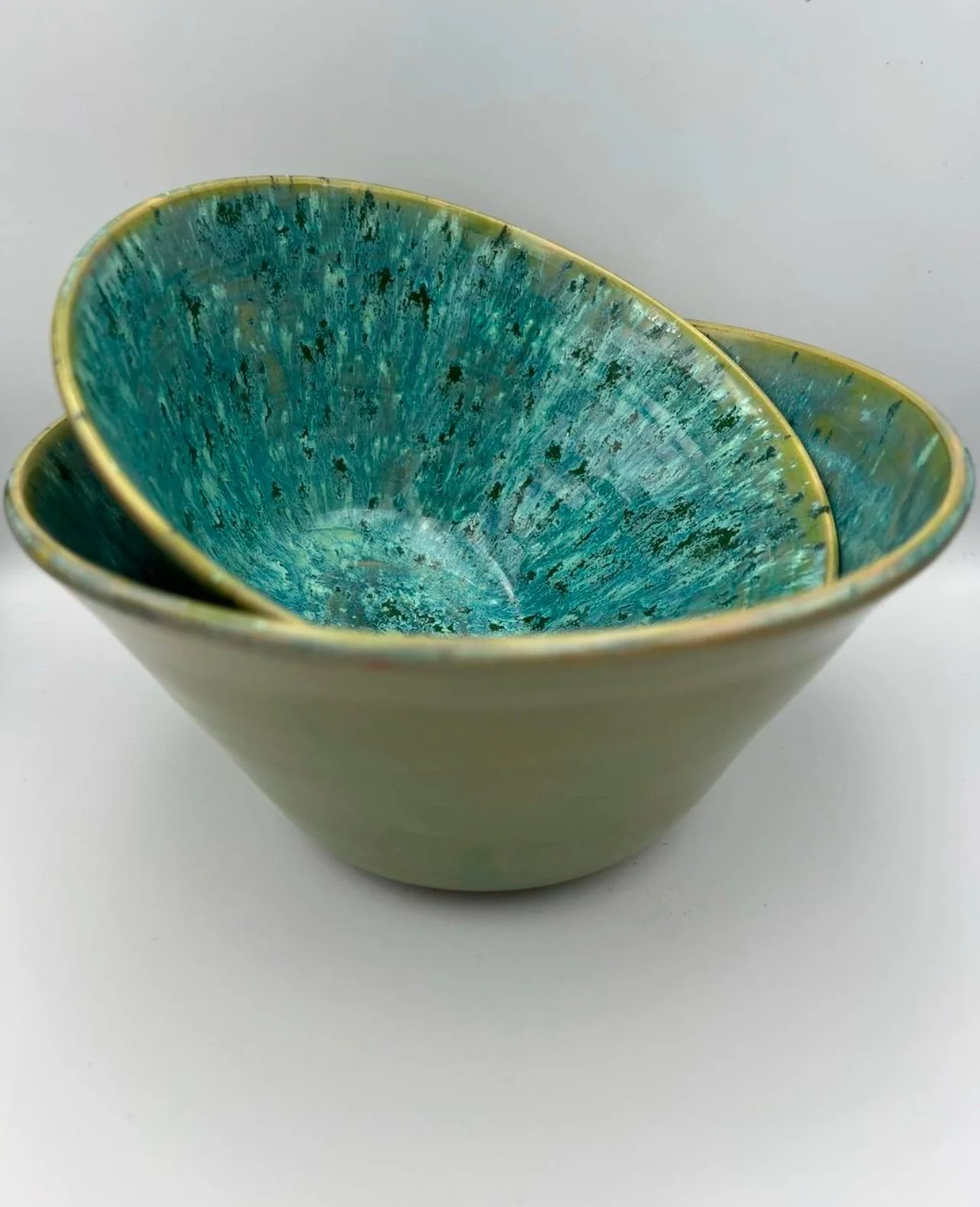 Drie gestapelde keramieken kommen met groene en blauwe glazuur, op een witte achtergrond.