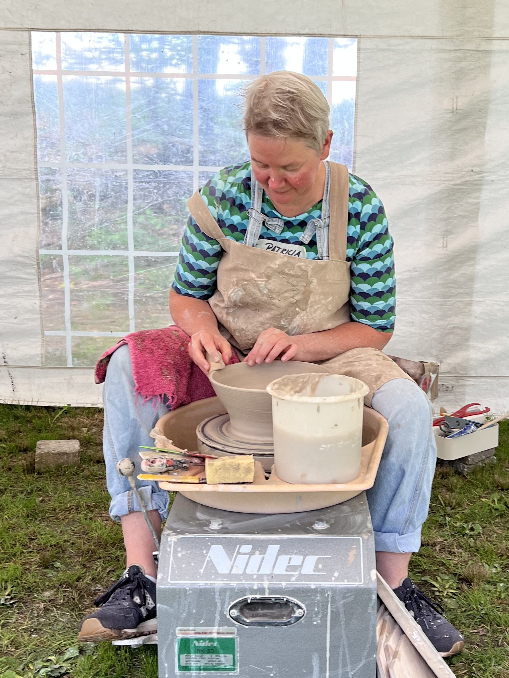 Vrouw die pottenbakken doet op een pottenbakkerswiel in een tent.