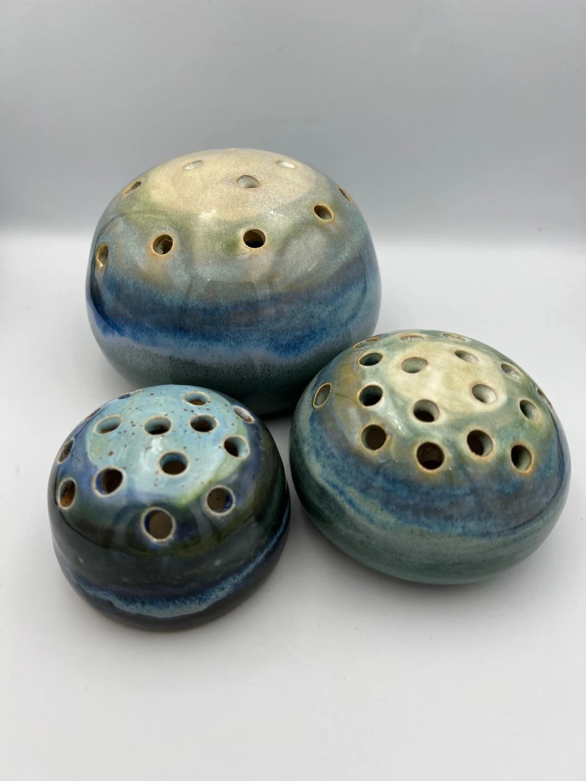 Drie keramische keramische klankschalen met perforaties en blauwe, groene en beige glazuur.