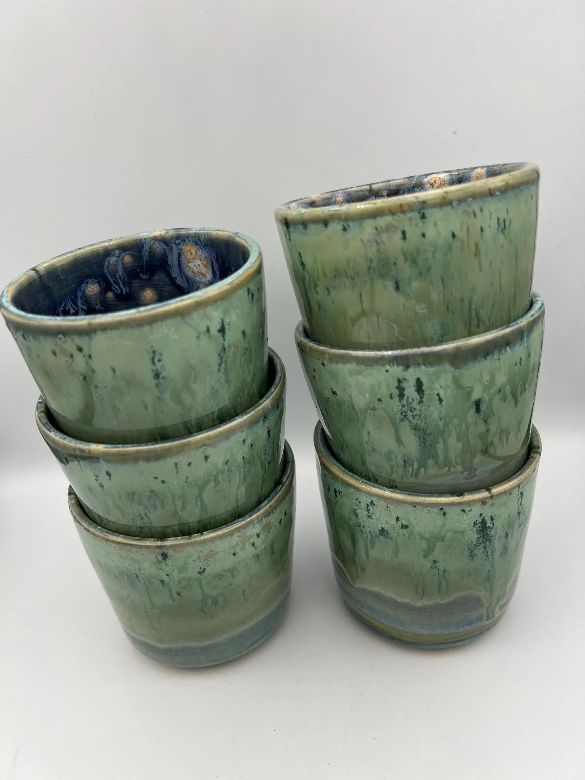 Een stapel van acht groene keramieken potten met blauwe binnenzijde op een witte achtergrond.